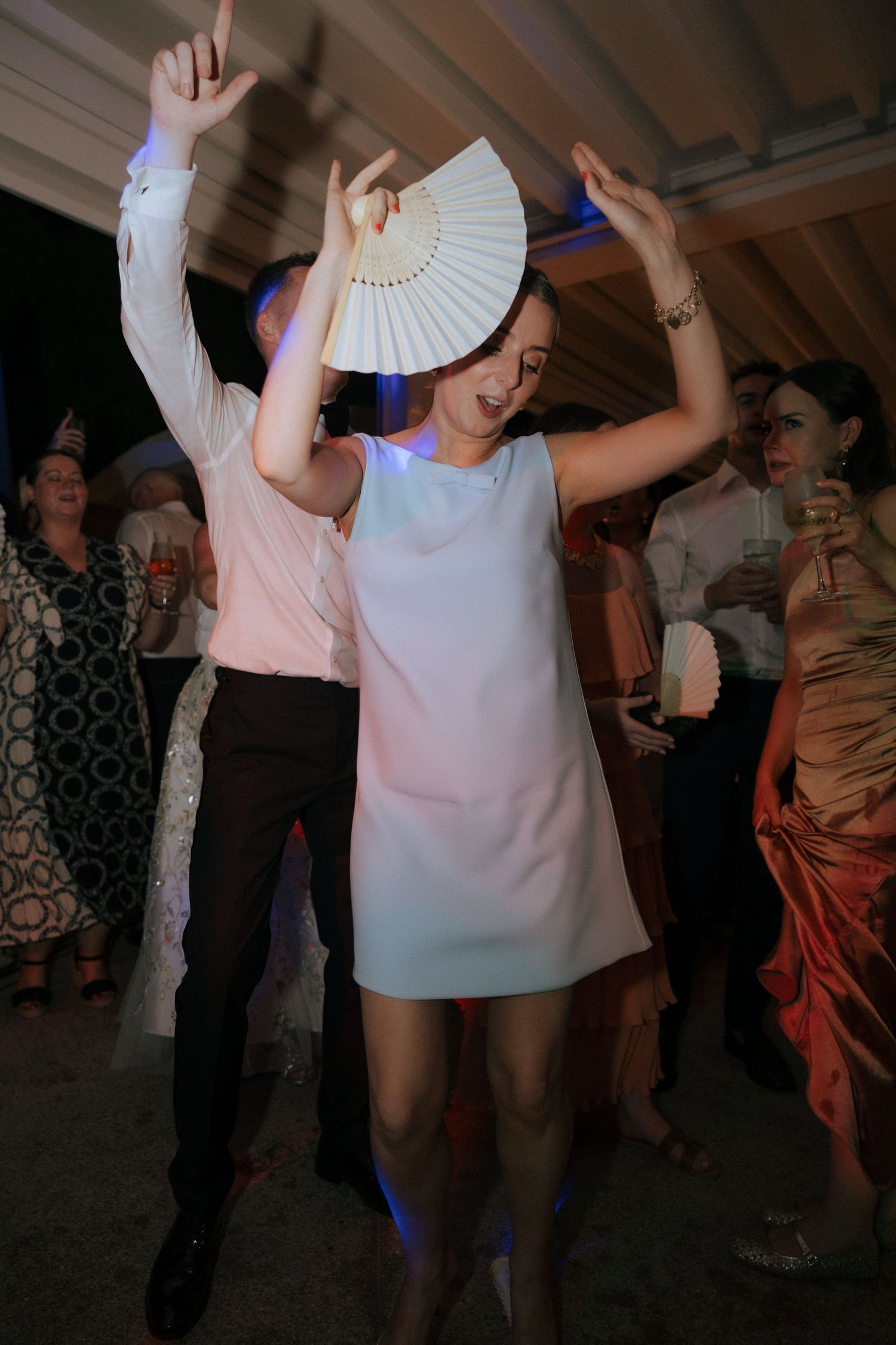 Wedding guests dance with white paper fans during an evening reception celebration.