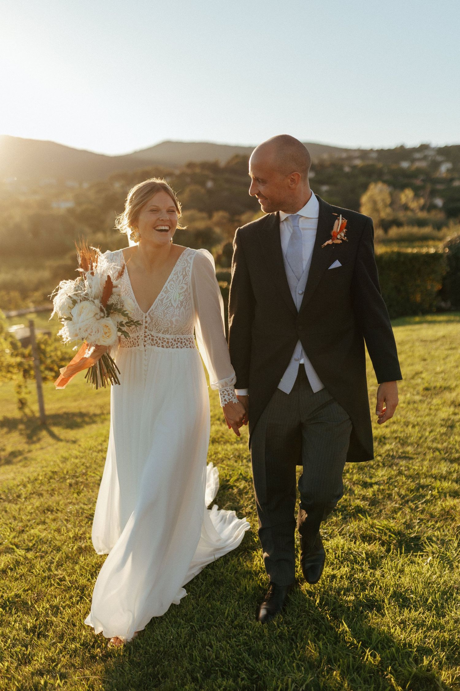 A couple walks together on a grassy hilltop during their sunset wedding celebration.