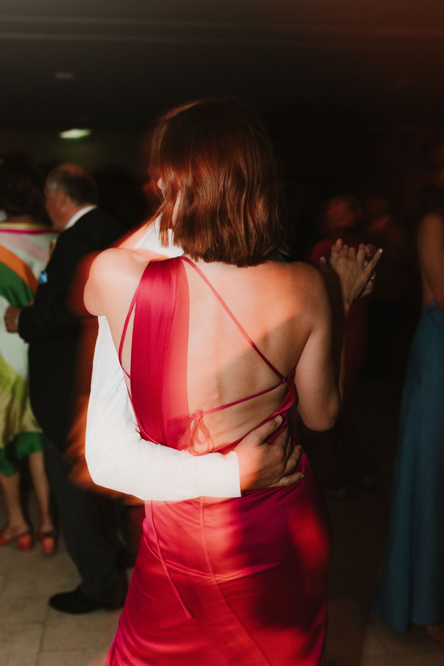 Woman in red formal dress with strappy back design dances at evening event.