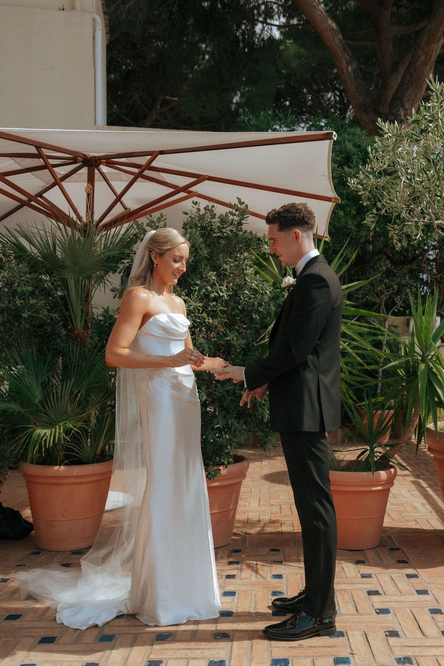 First look wedding moment on garden terrace with tropical plants and terracotta tiles.