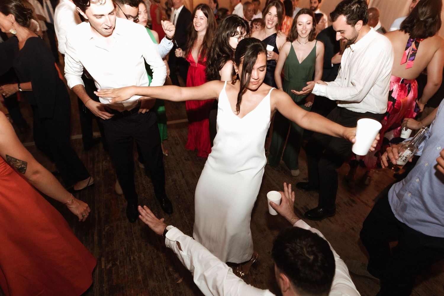 On a dance floor, partygoers celebrate while someone in a white gown dances in the middle of the jubilant crowd.