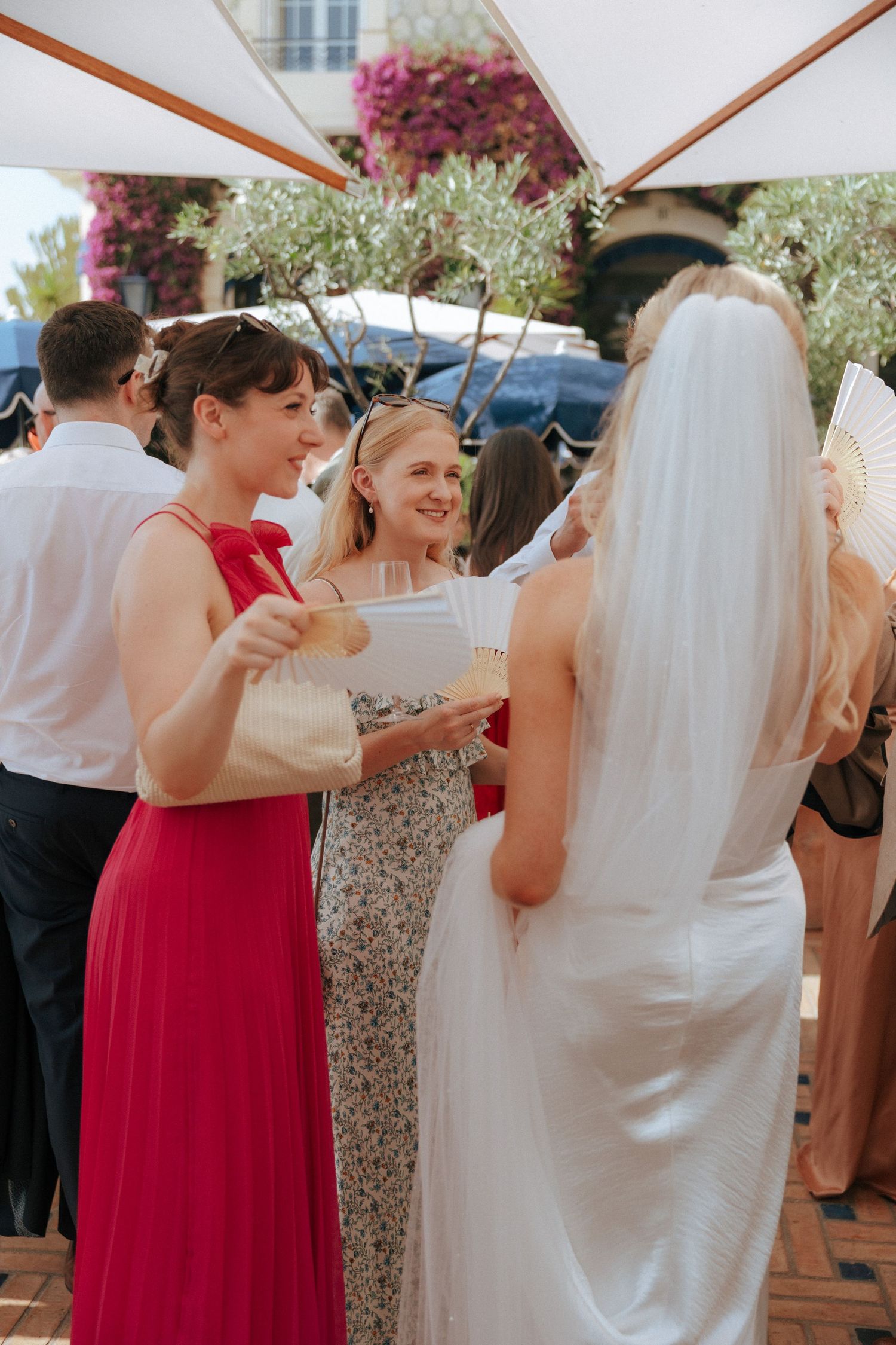 Wedding guests in colorful attire mingling under white umbrellas at an outdoor reception.