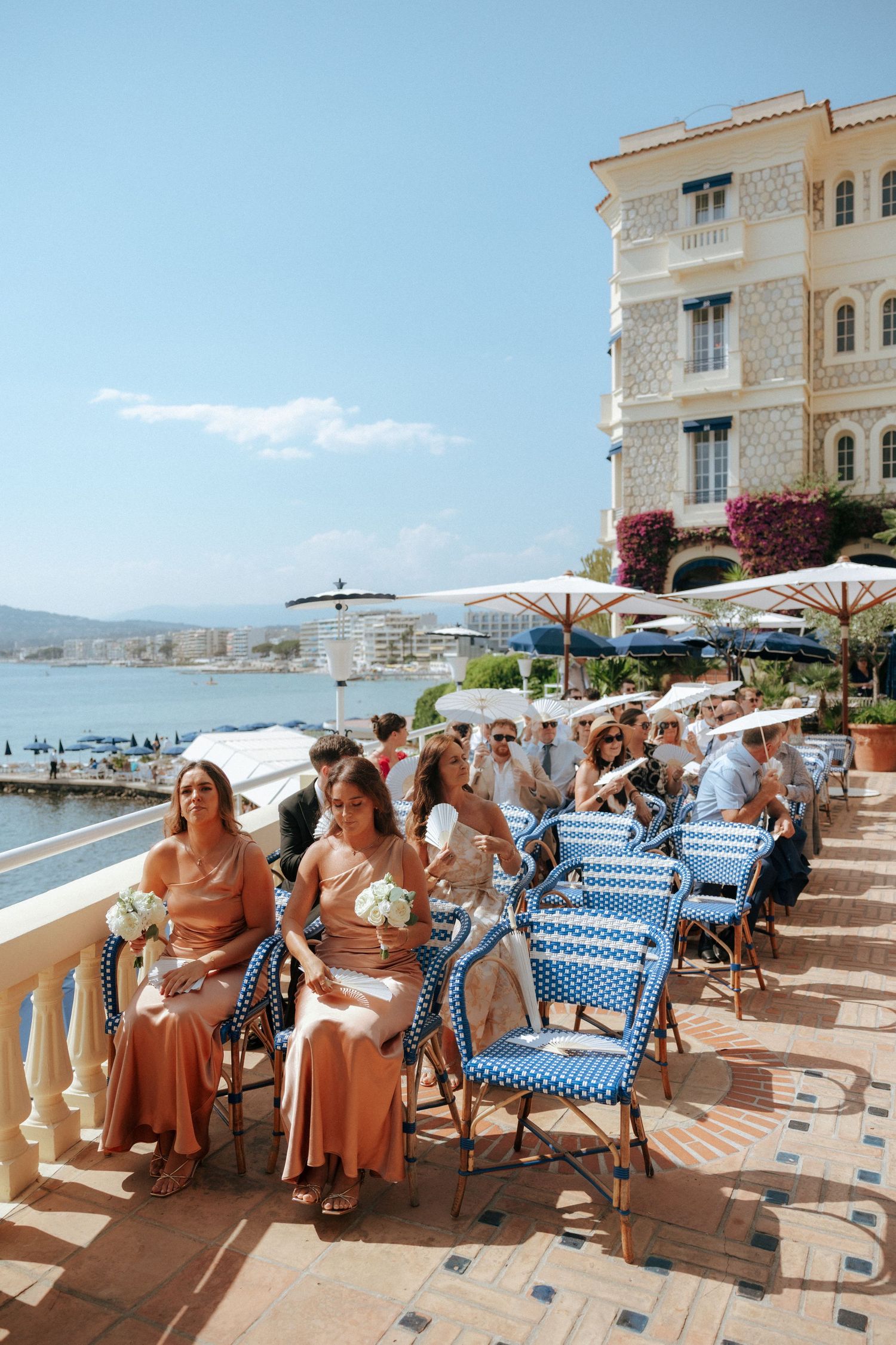 Wedding guests relaxing on a Mediterranean terrace with blue chairs and white umbrellas.