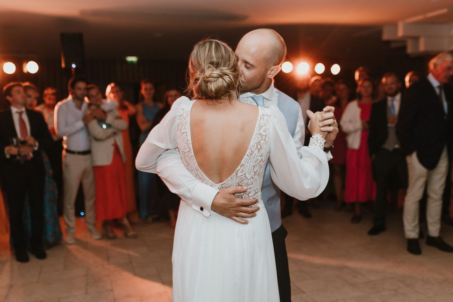 Couple sharing their first dance at wedding reception with guests watching in background.