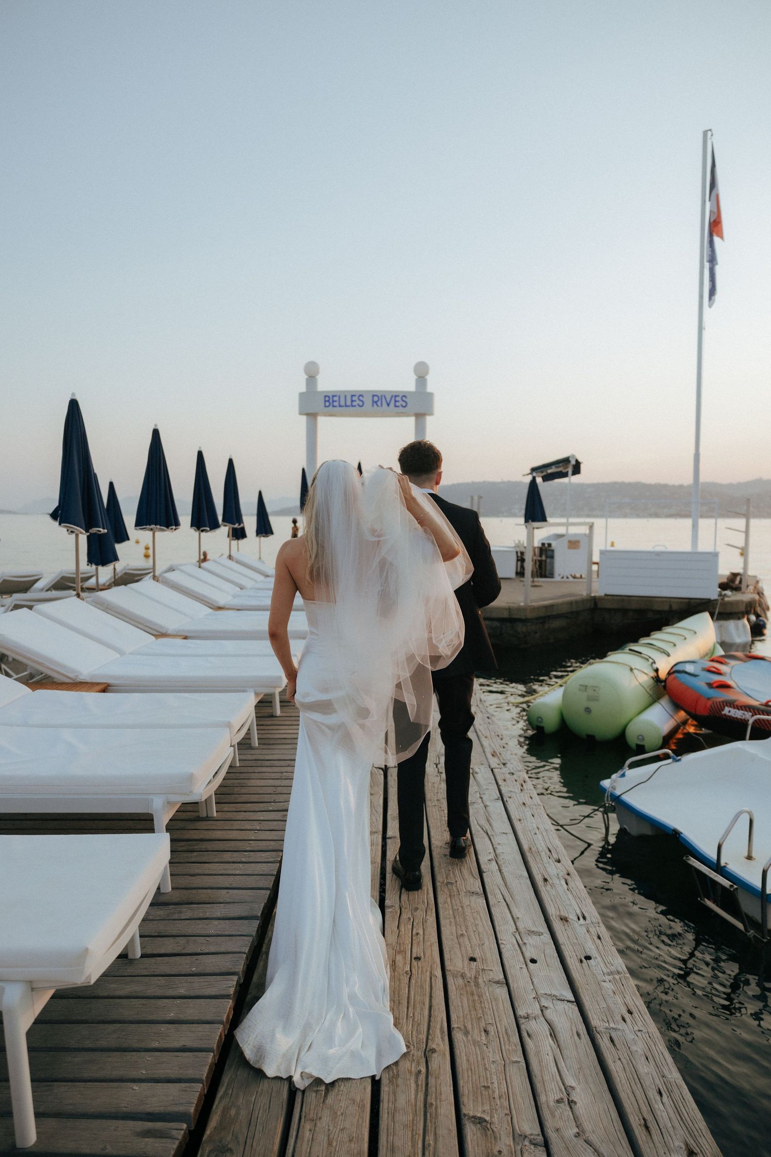 Couple in wedding attire posing for photos on a wooden dock by the water.