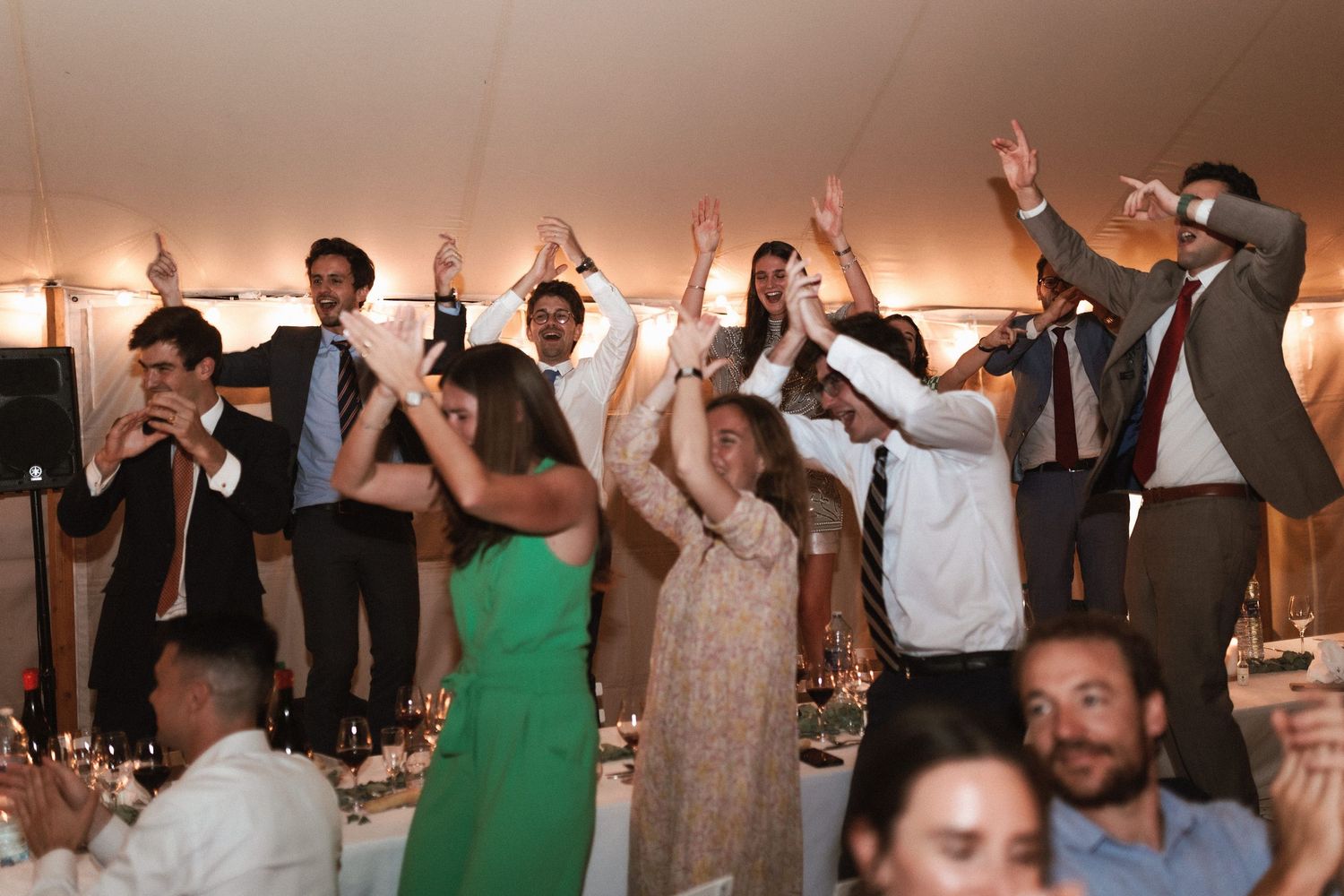 Wedding guests dance with their hands raised during a lively celebration under a tent reception.