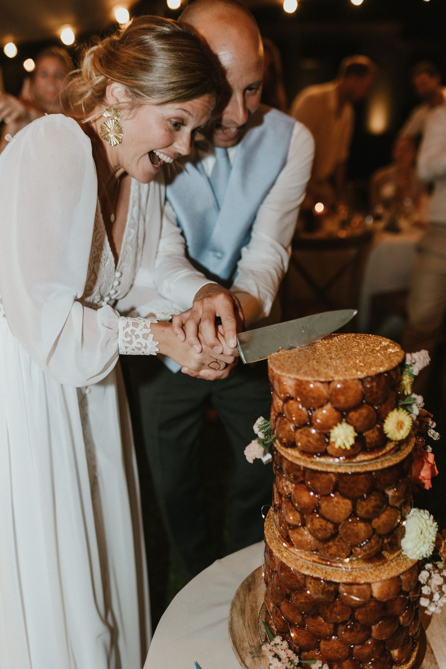A couple cutting their rustic three-tiered wedding cake decorated with flowers.