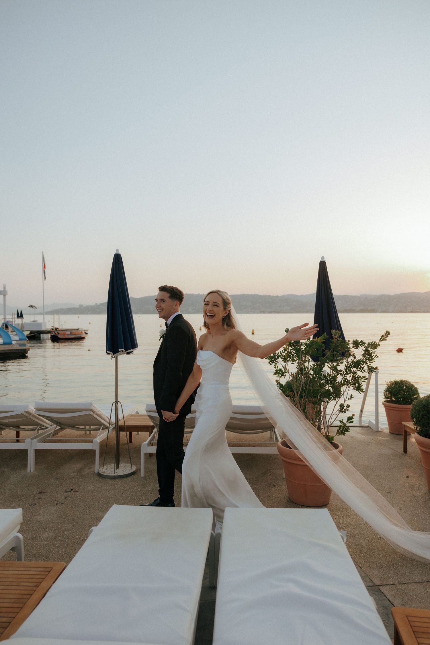 A bride's dress train dramatically flows across a sunset beach boardwalk.