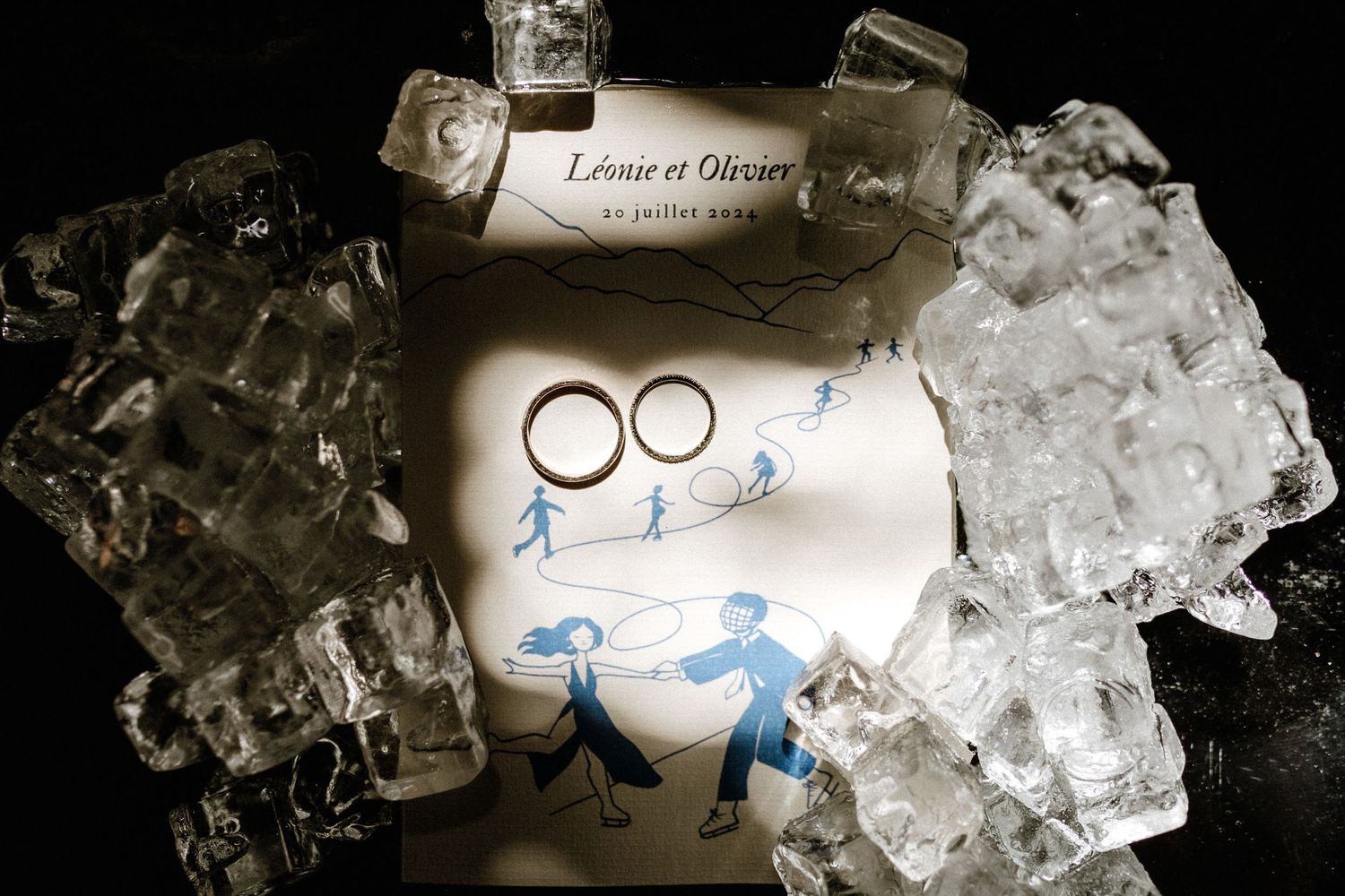 Wedding rings artistically placed on ice with hand-drawn figures.