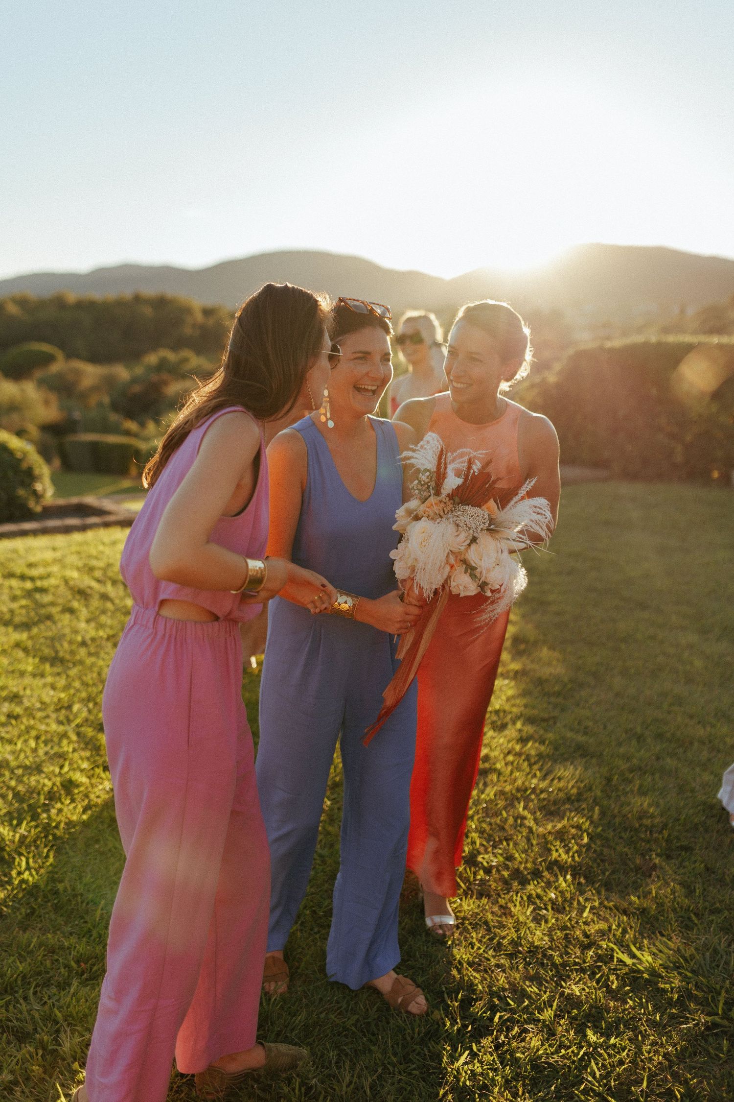 Wedding party in colorful dresses shares joyful moment at sunset in countryside setting.