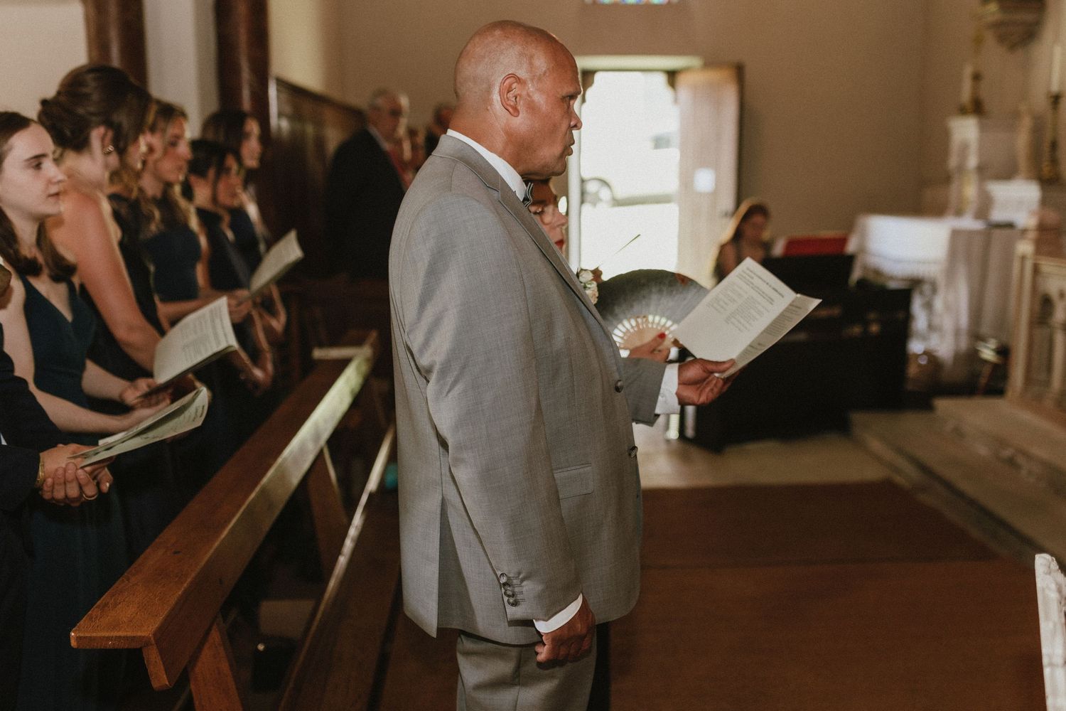 Wedding ceremony attendees following along with programs in a traditional church setting.