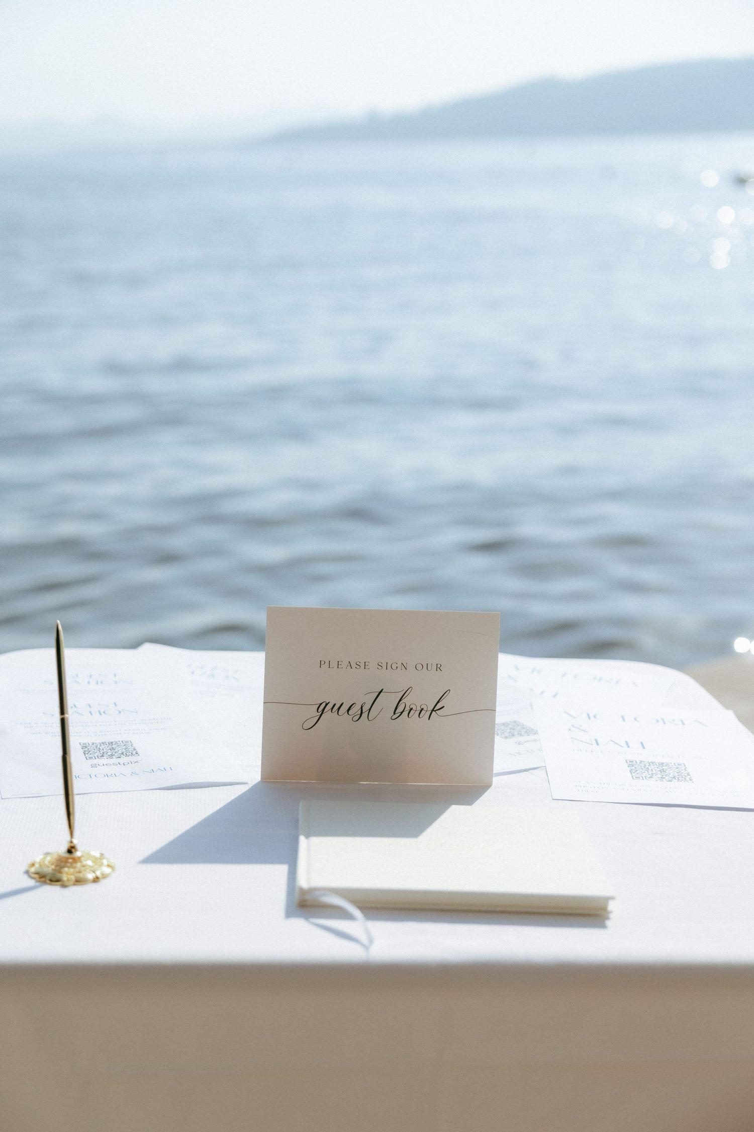 Place cards with elegant calligraphy sitting on a white table with ocean waves visible in background.