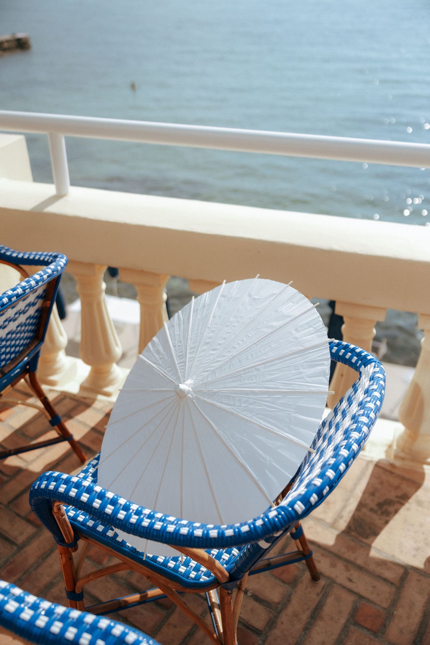 White parasols and blue patterned chairs on a sunny oceanfront terrace.