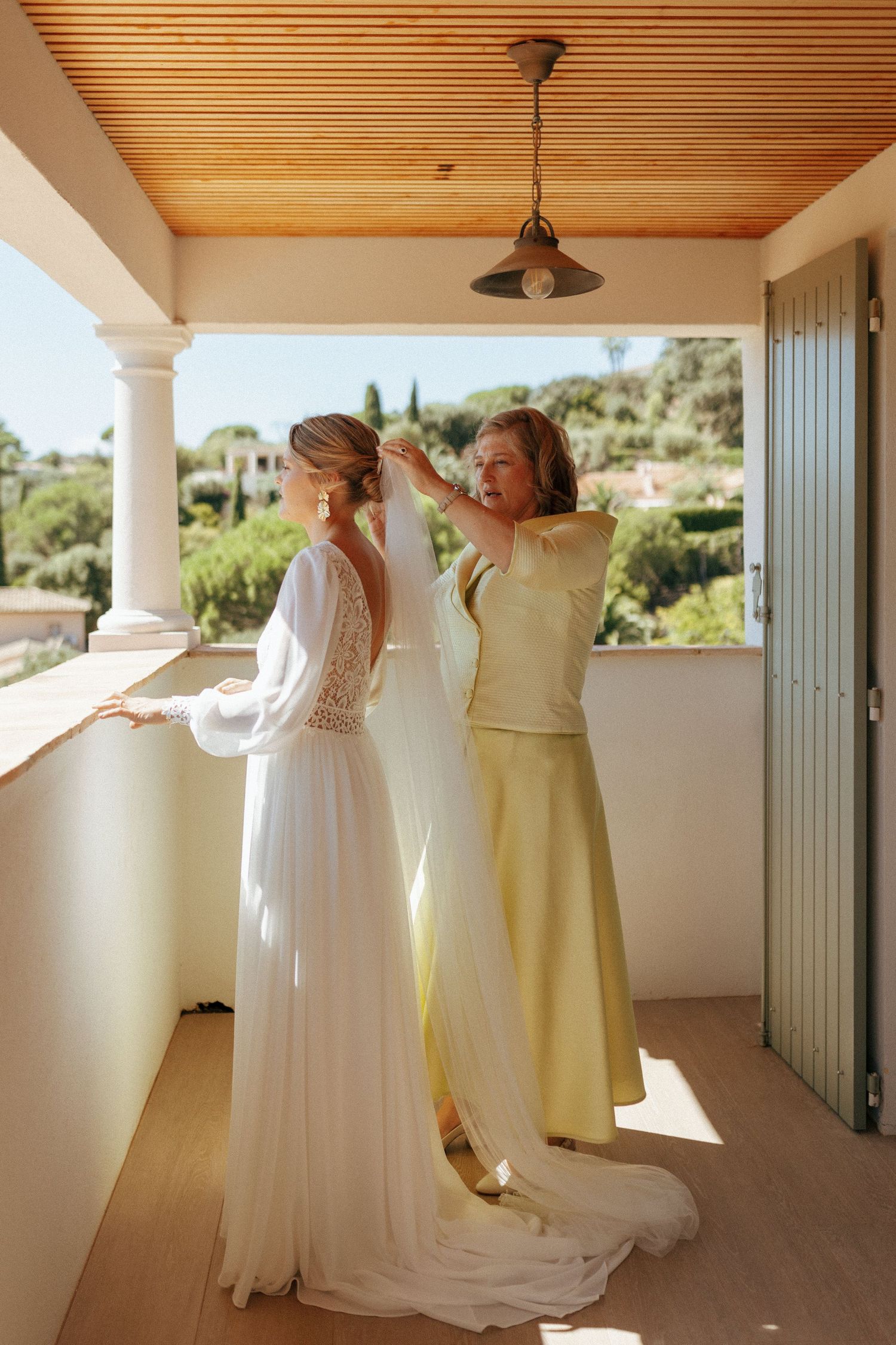 Final wedding dress adjustments on a sunny Mediterranean-style balcony.