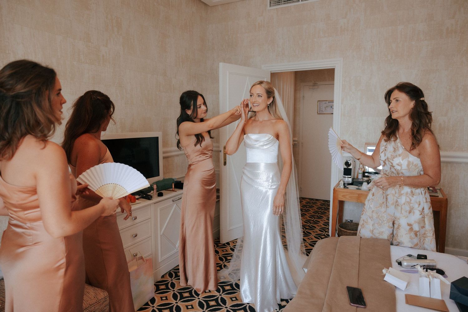 Several candid moments show women in formal dresses getting ready before a special event in a neutral-toned room.