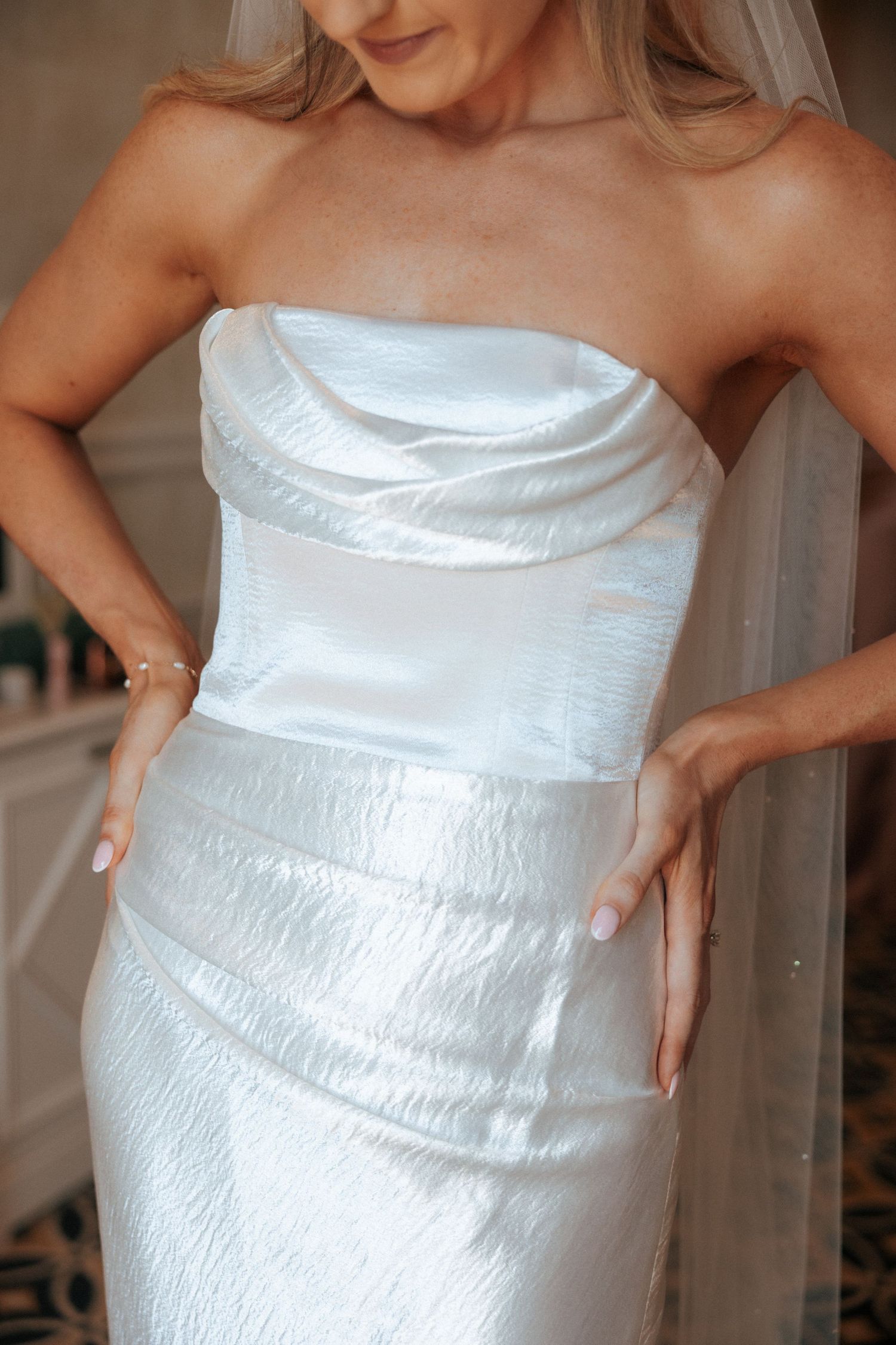 Close-up detail of a strapless white wedding gown with ruched satin fabric and textured detailing.