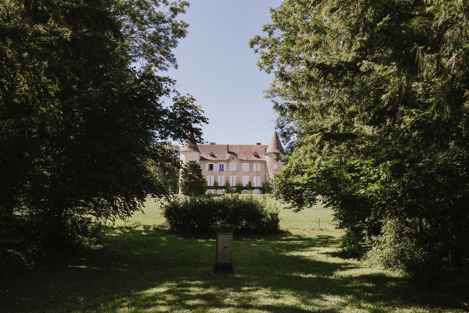 A grand chateau viewed through a tree-lined lawn path in bright daylight.