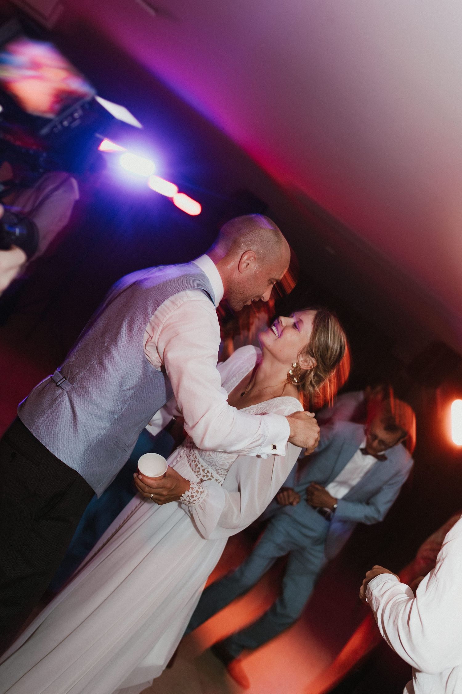 Wedding couple dips dramatically during dance under purple and blue lighting.