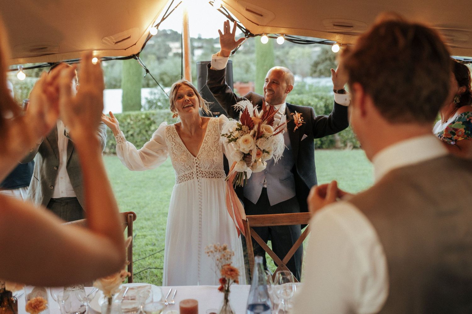 Joyful wedding celebration under a tent as the newlyweds raise their hands in celebration during the reception.