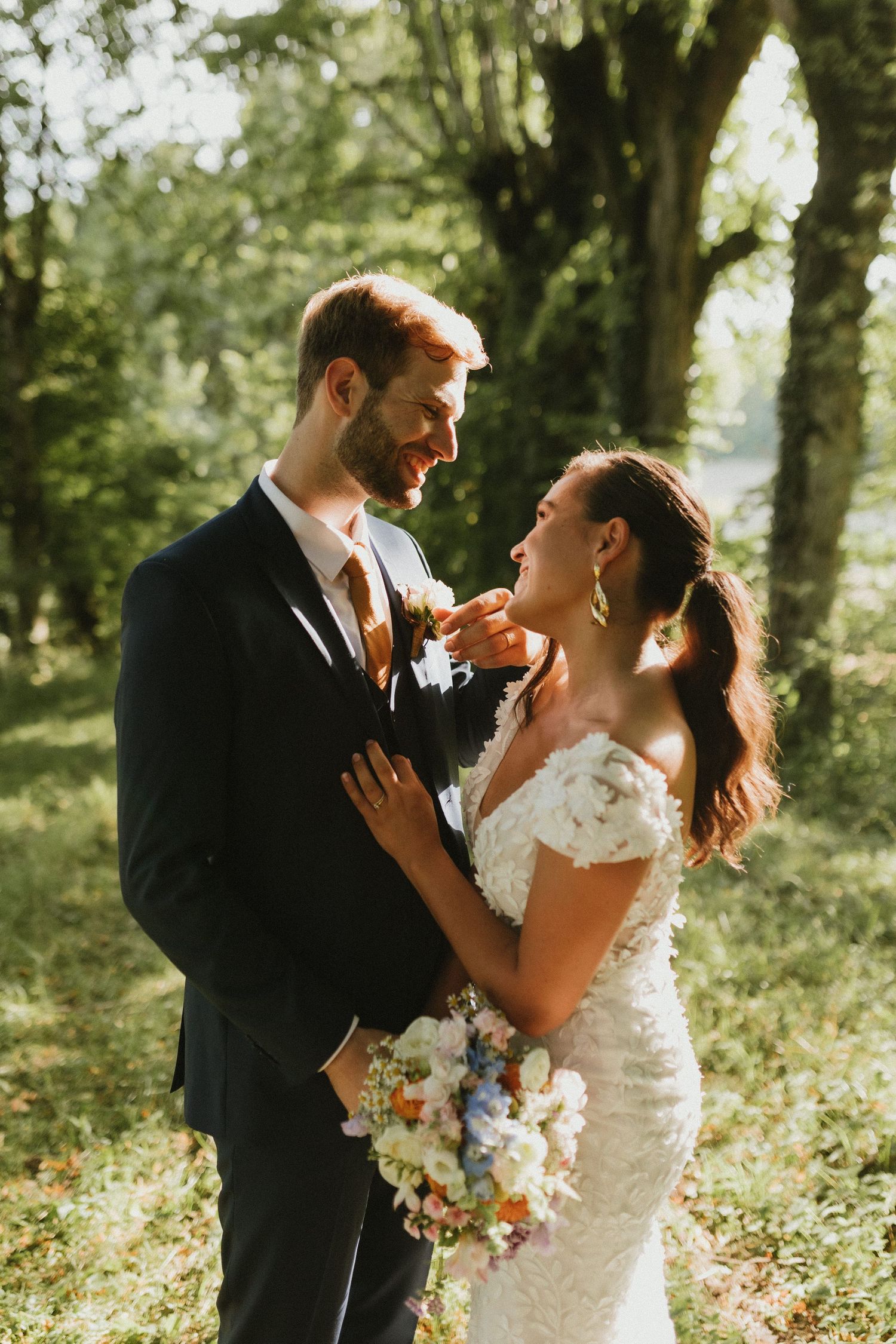 Wedding couple sharing a romantic moment in dappled sunlight beneath trees.