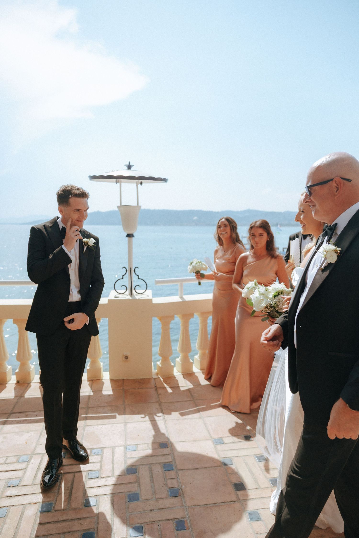 Wedding party gathered on a seaside terrace with white balustrade and ocean views.