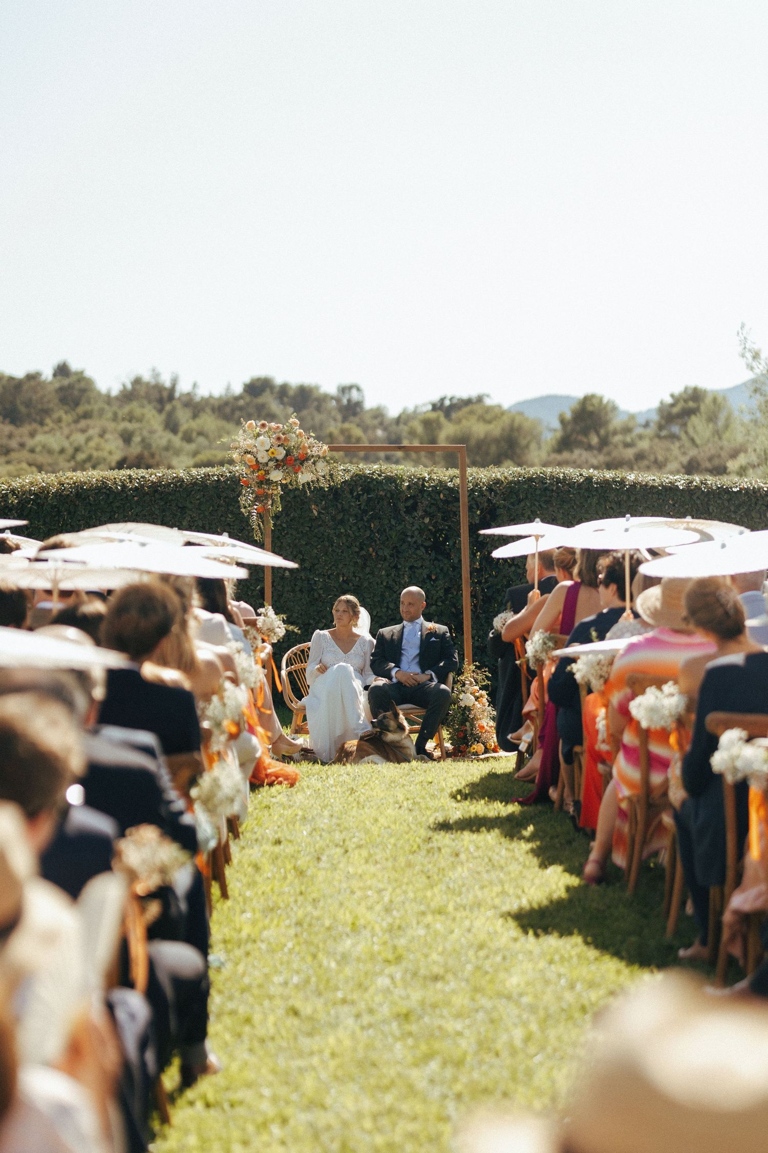 Outdoor wedding ceremony with rows of guests seated on a sunny lawn with mountains in the background.