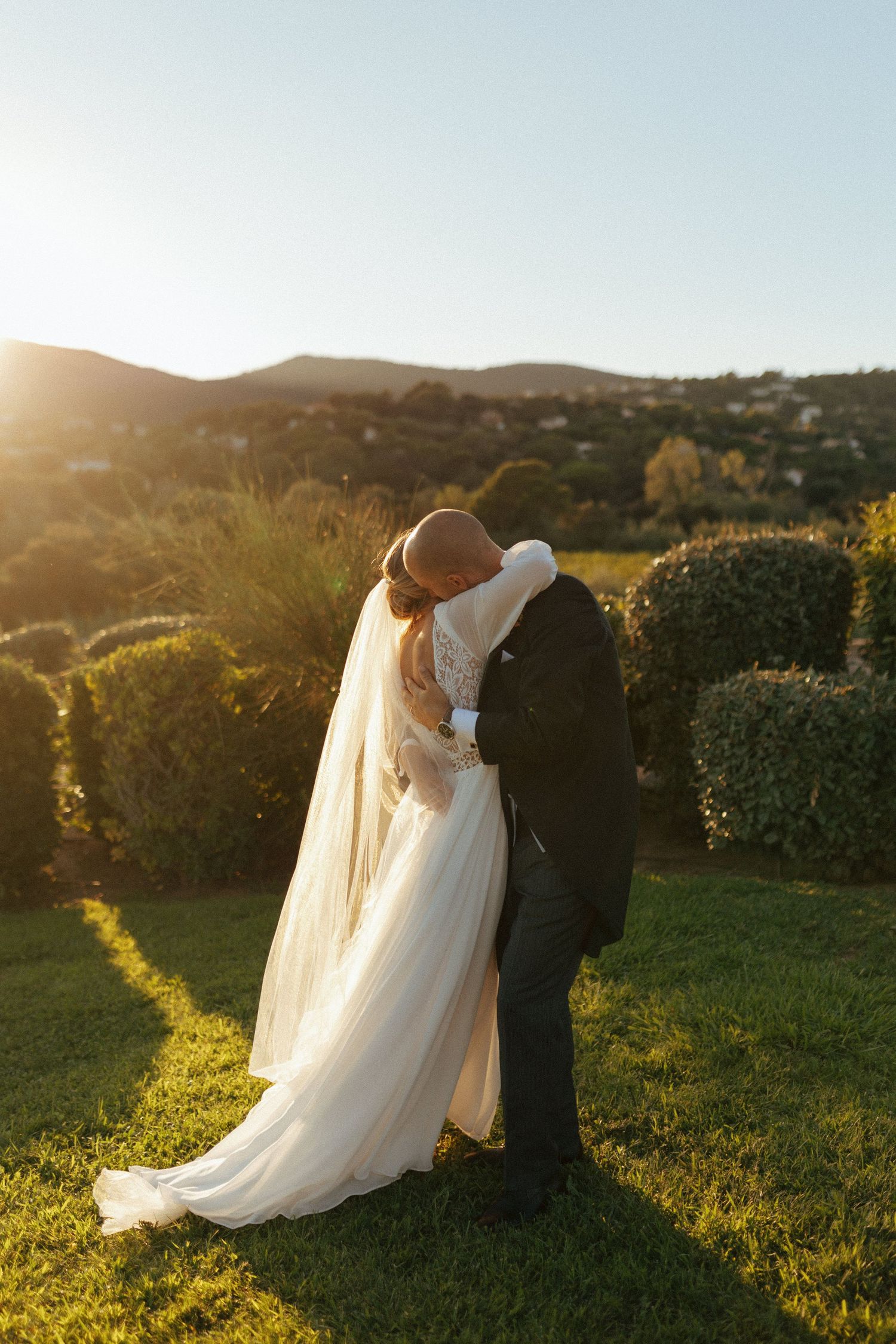 A romantic golden hour wedding portrait of a couple embracing on a hilltop.