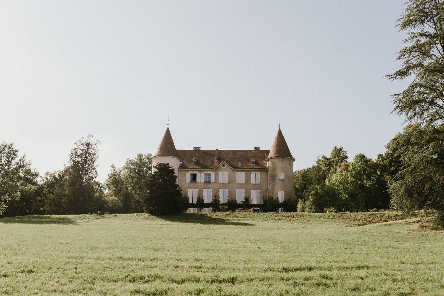 A majestic French chateau with twin turrets stands proudly on a vast green lawn.
