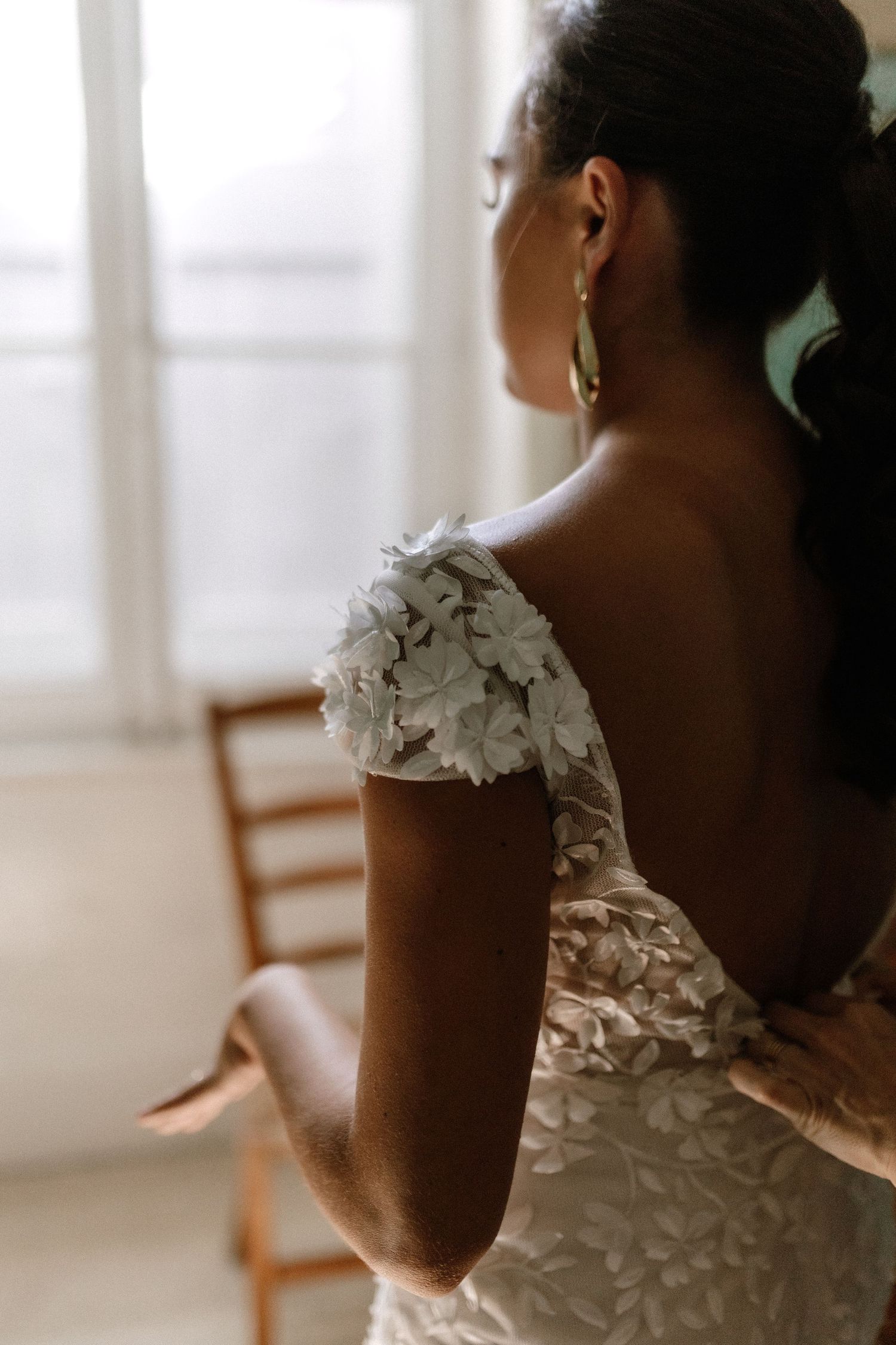 Elegant white floral wedding dress with delicate shoulder detail captured in soft window light.