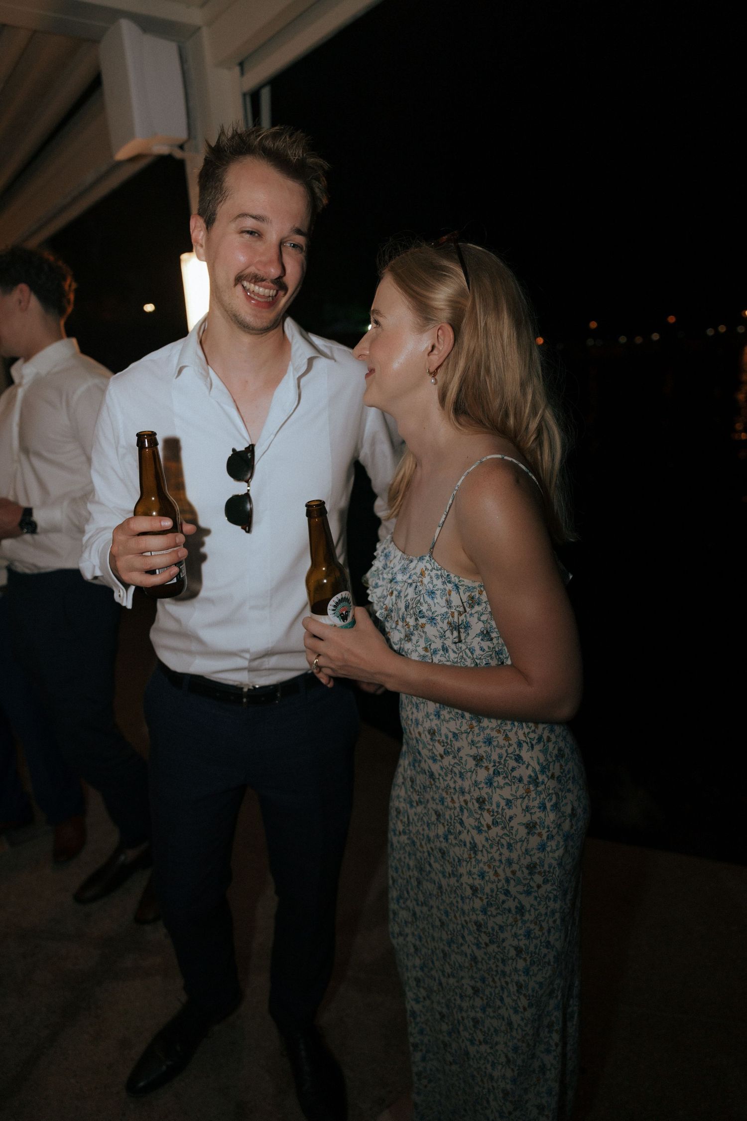 Party guests enjoying drinks and conversation on an outdoor patio at night.