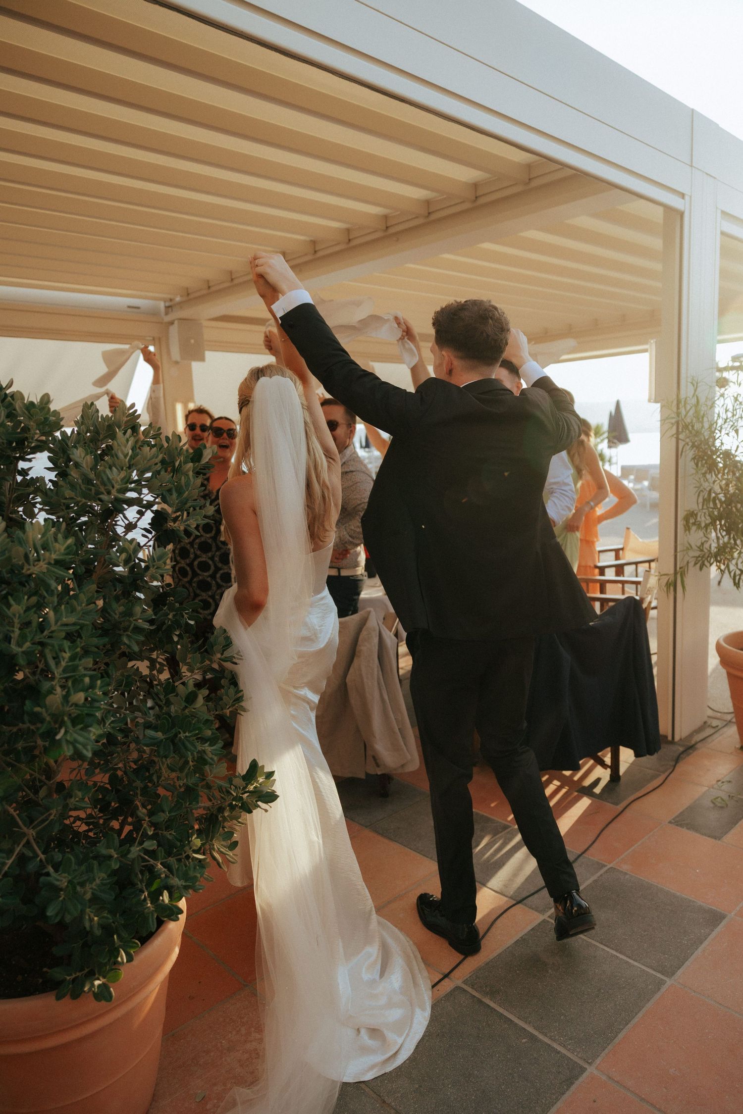 Wedding guests dance and celebrate on an outdoor covered patio during golden hour.