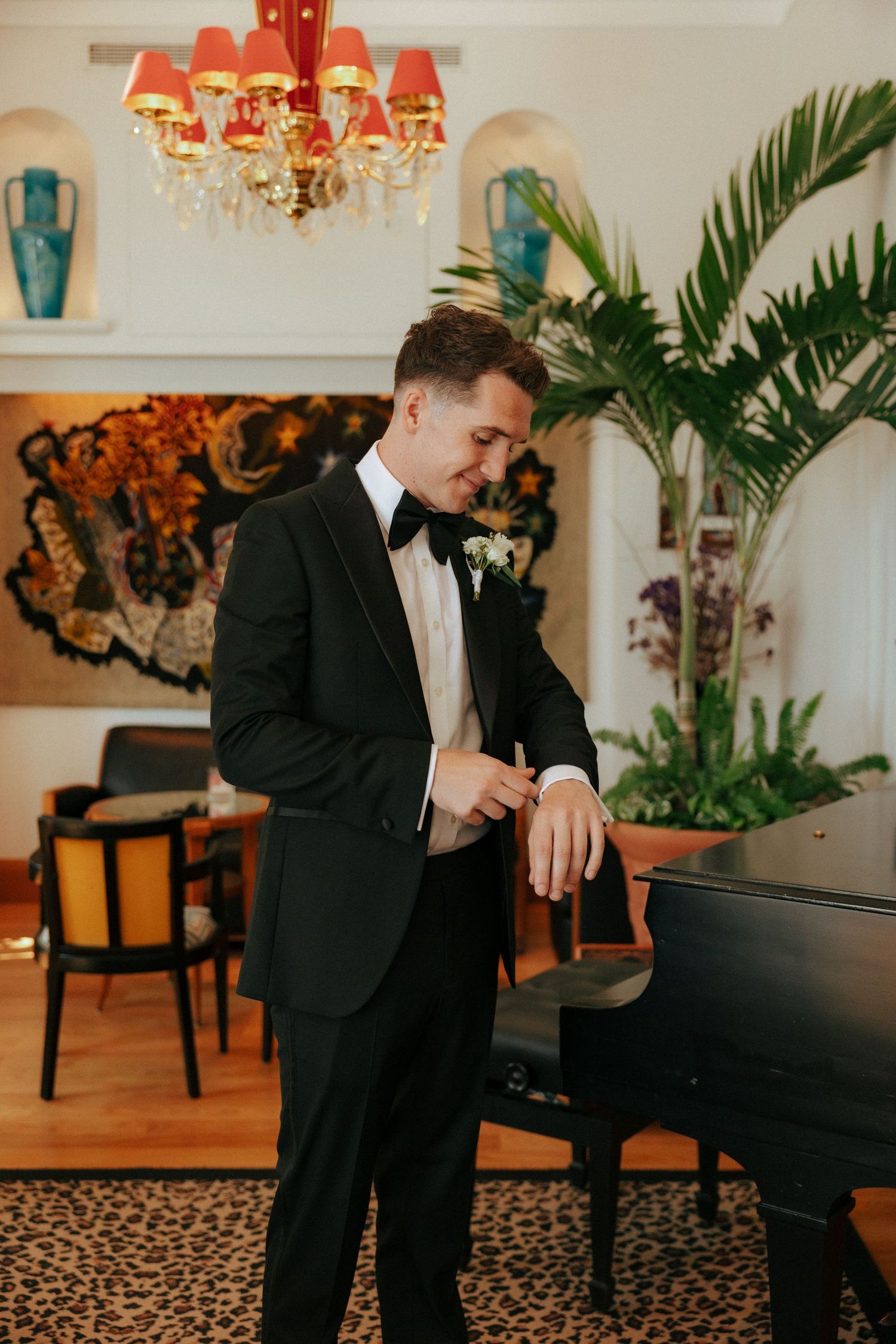 A tuxedo-clad man in an elegantly decorated room with red lampshades and tropical plants.