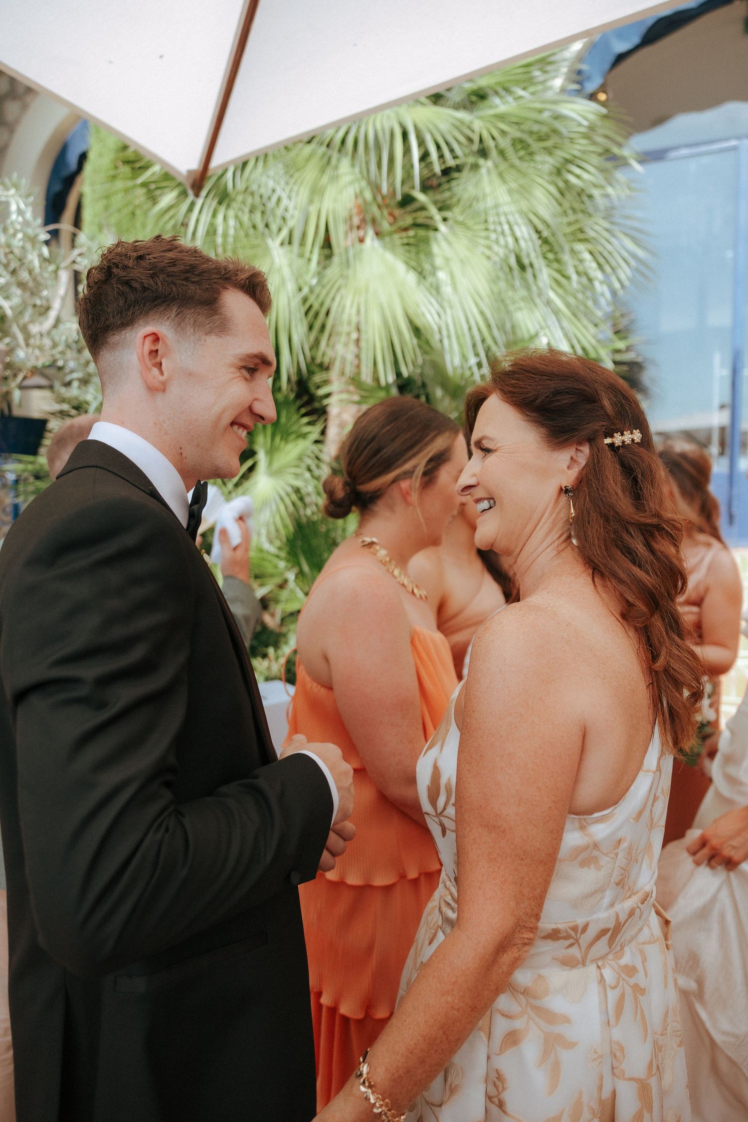 Wedding party members share joyful moments under palm trees at an outdoor venue.