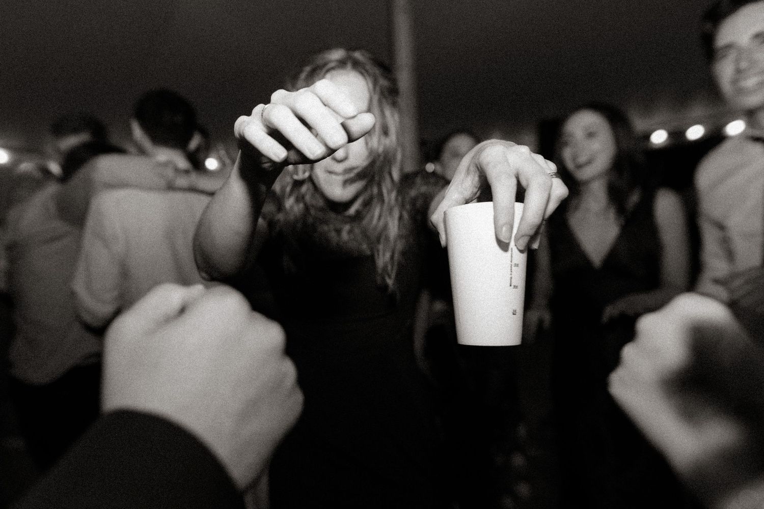 People toasting with plastic cups at a crowded nighttime party in black and white.