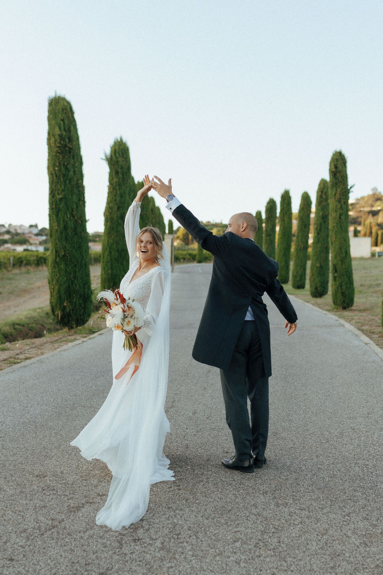 Wedding couple dancing and twirling on a cypress-lined driveway at dusk.