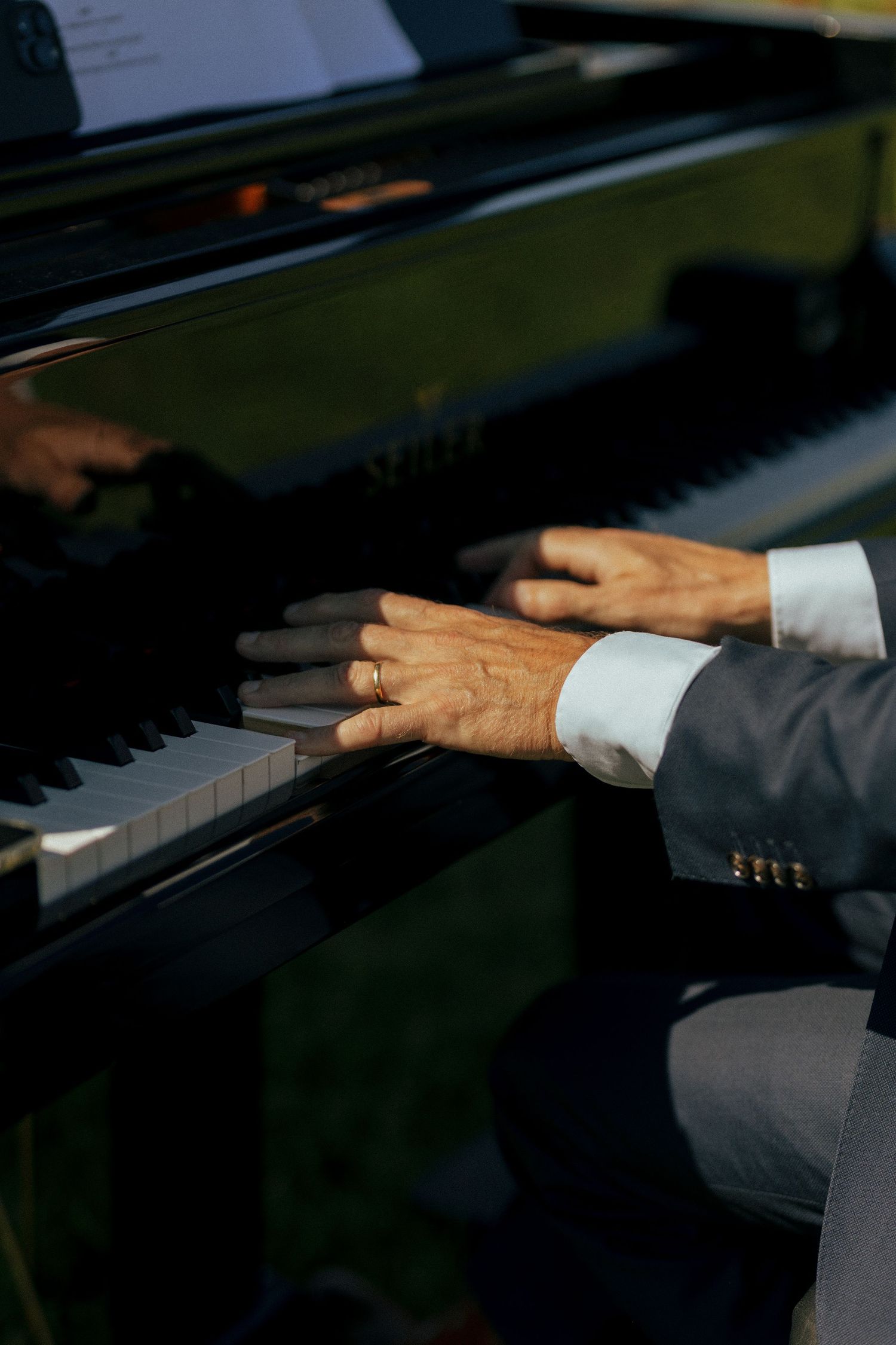 Close-up of hands with wedding ring playing piano keys in dramatic lighting.