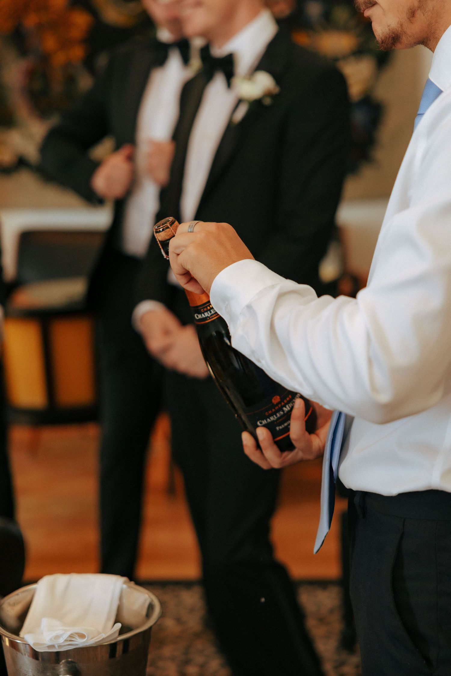 Wedding party members opening champagne bottles during pre-ceremony preparations.