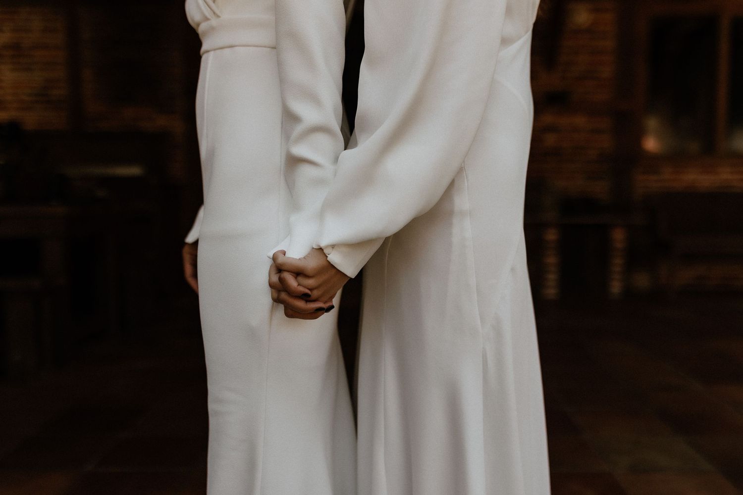 Close-up of two people wearing elegant white wedding attire holding hands in a romantic embrace during ceremony.