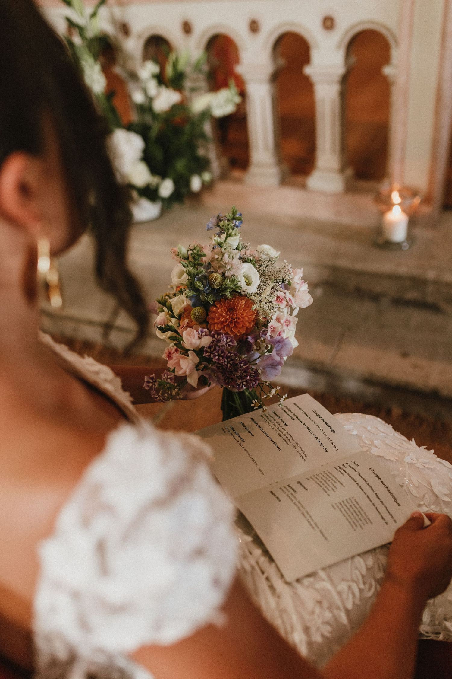 Close up of wedding program and floral arrangement with candles in church setting.