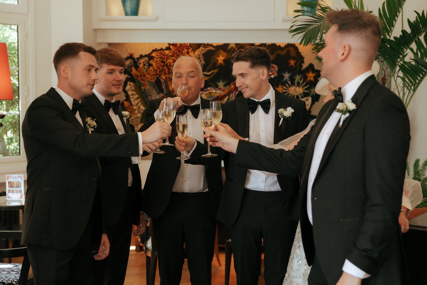 A group of groomsmen in black tuxedos toast with champagne glasses during a wedding celebration.