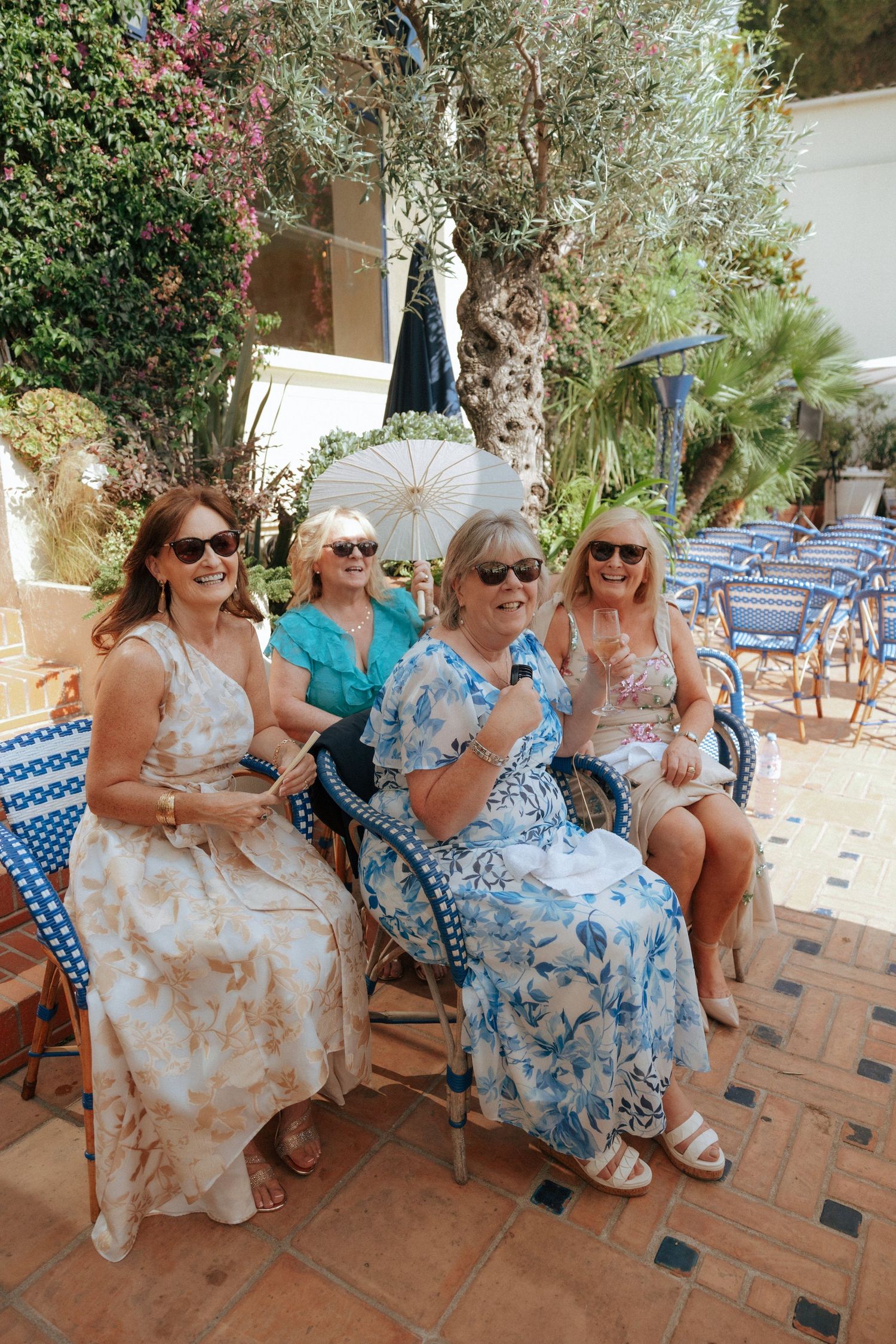 Wedding guests in summer dresses relaxing on blue chairs at an outdoor venue.