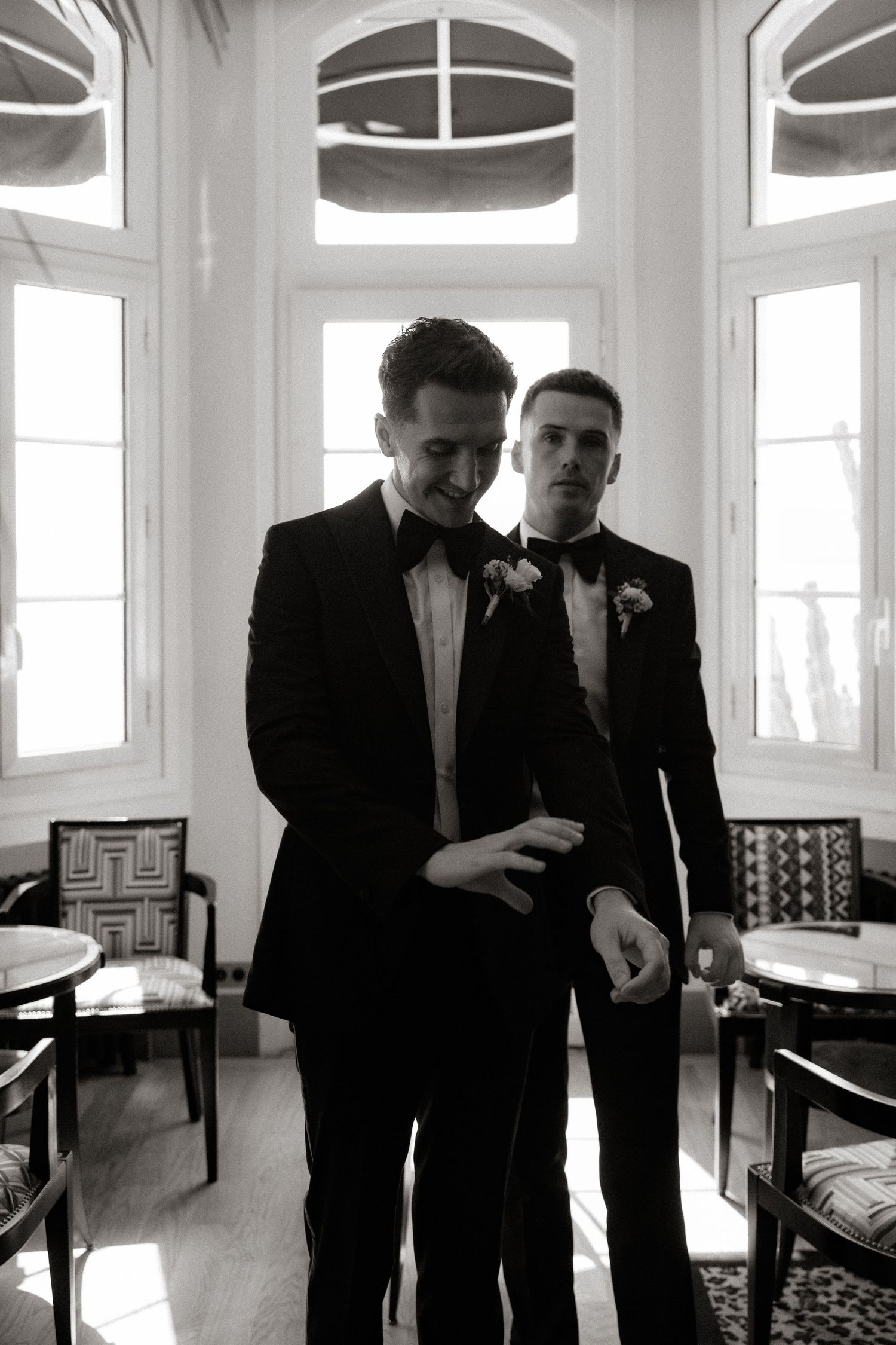 Groomsmen in black tuxedos sharing a celebratory moment in a bright white room.