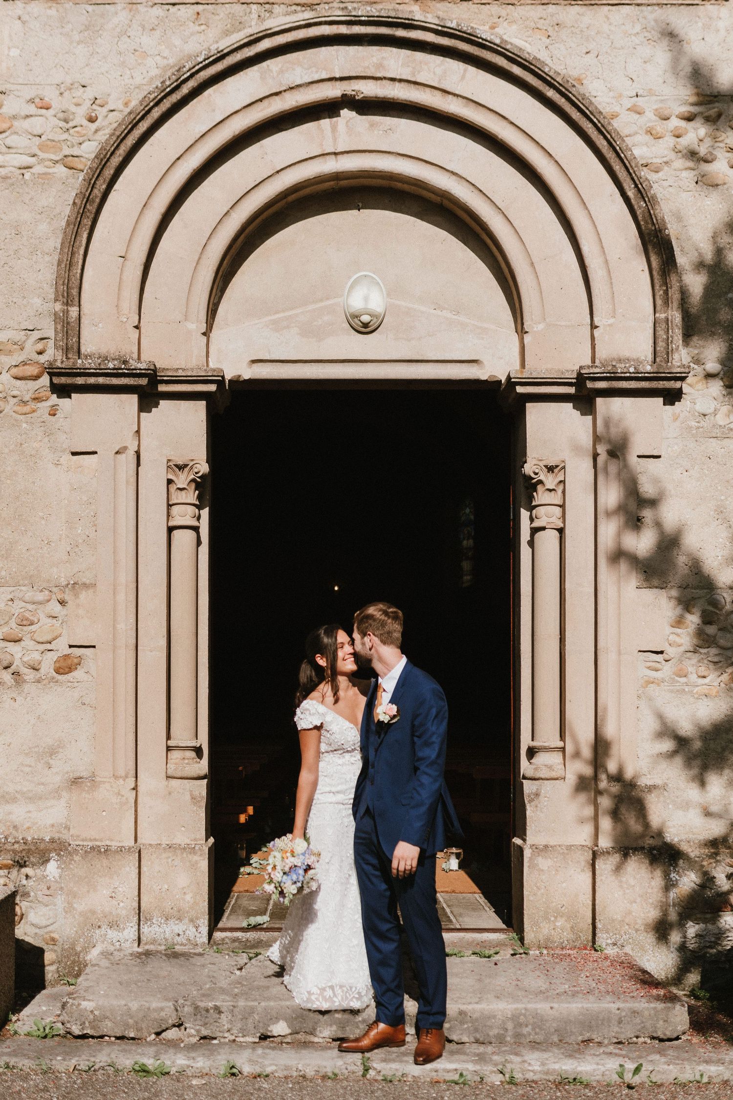 A couple stands in an arched stone doorway at a church during their wedding celebration.