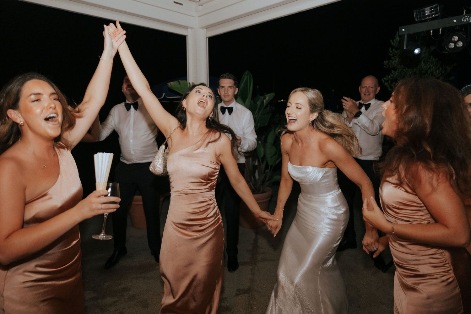 Wedding celebration on dance floor with bridesmaids in satin dresses dancing joyfully at reception.