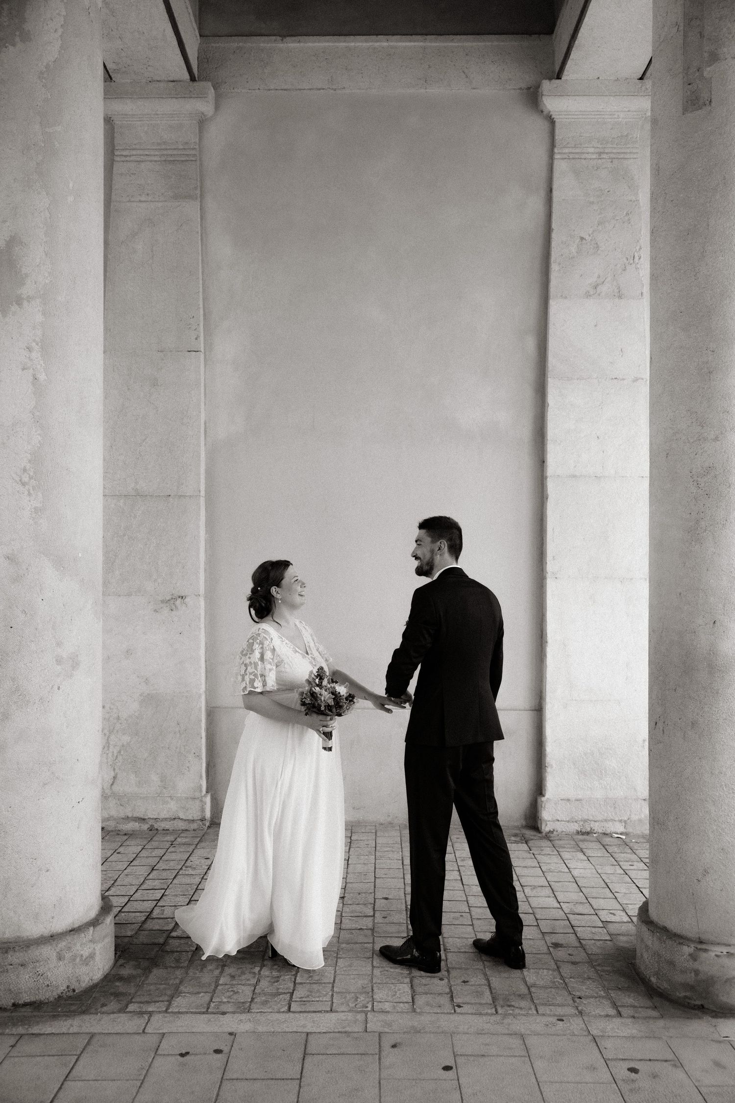 A classic black and white wedding photo of a couple standing between elegant stone columns.