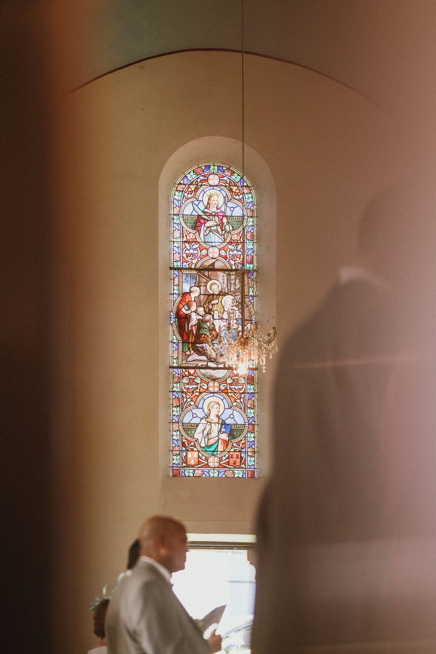 A stained glass church window with religious imagery glows above while a figure stands below.