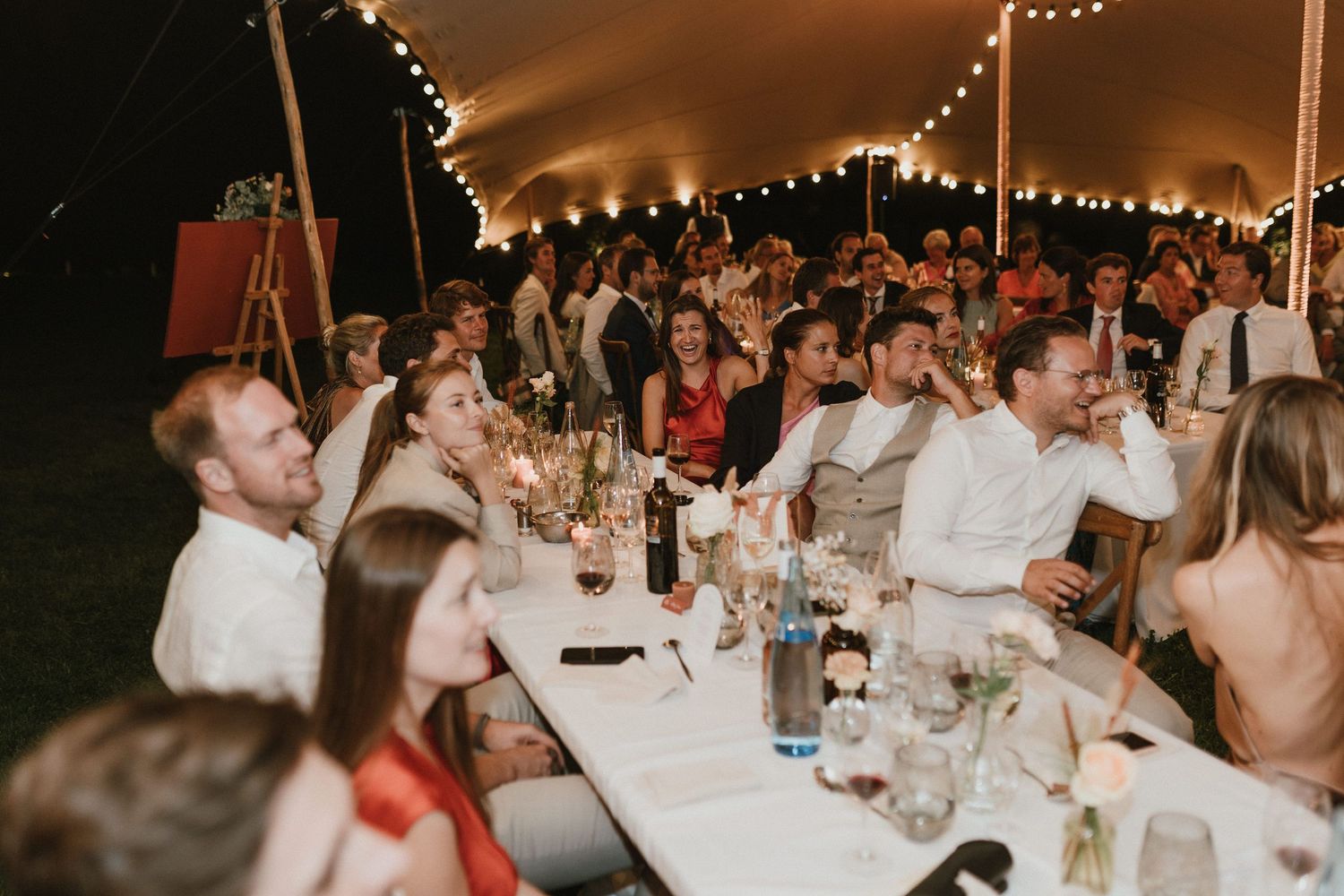 Wedding reception dinner under tent with string lights and guests seated at long tables.