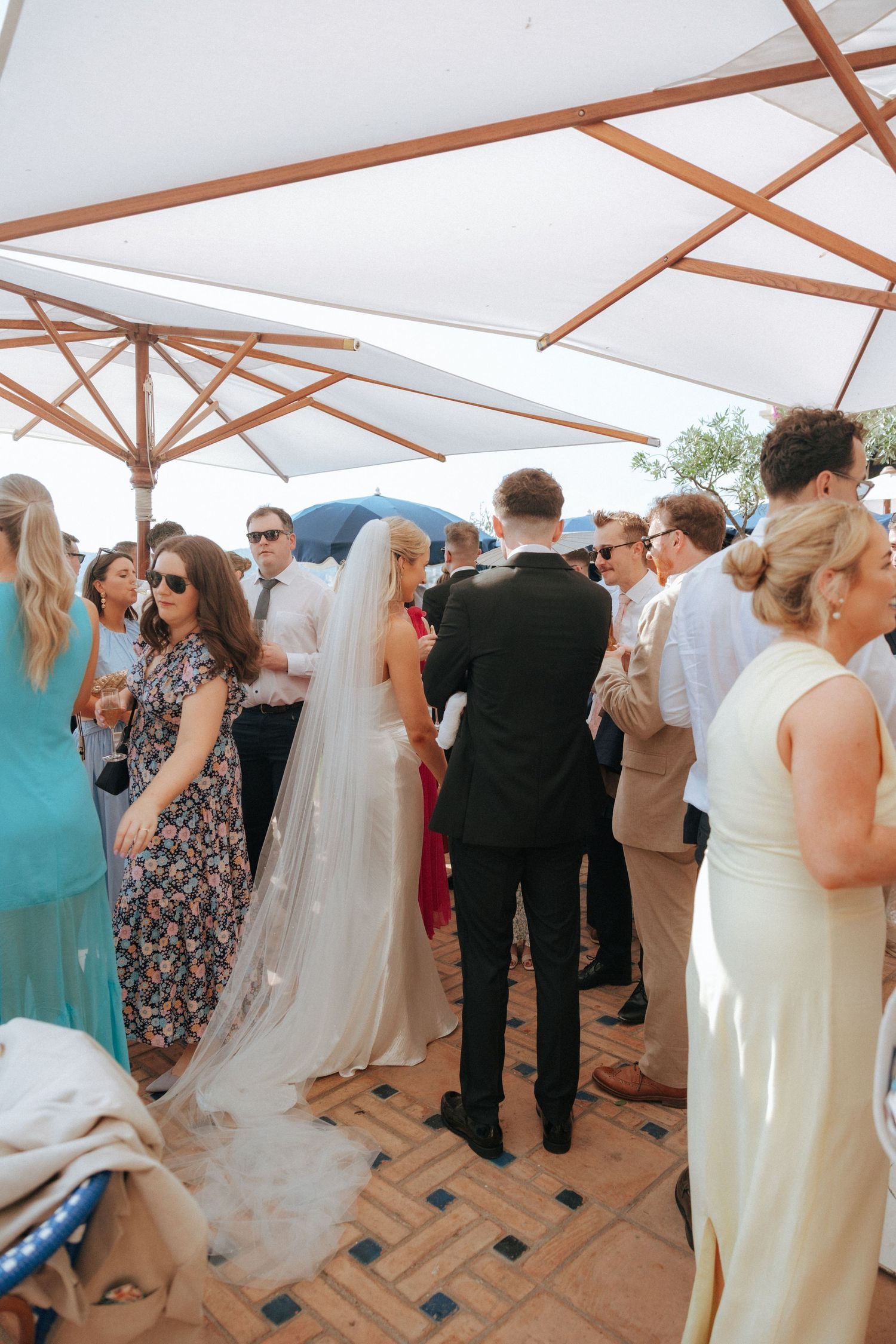Wedding reception gathering under white umbrellas on a tiled terrace.