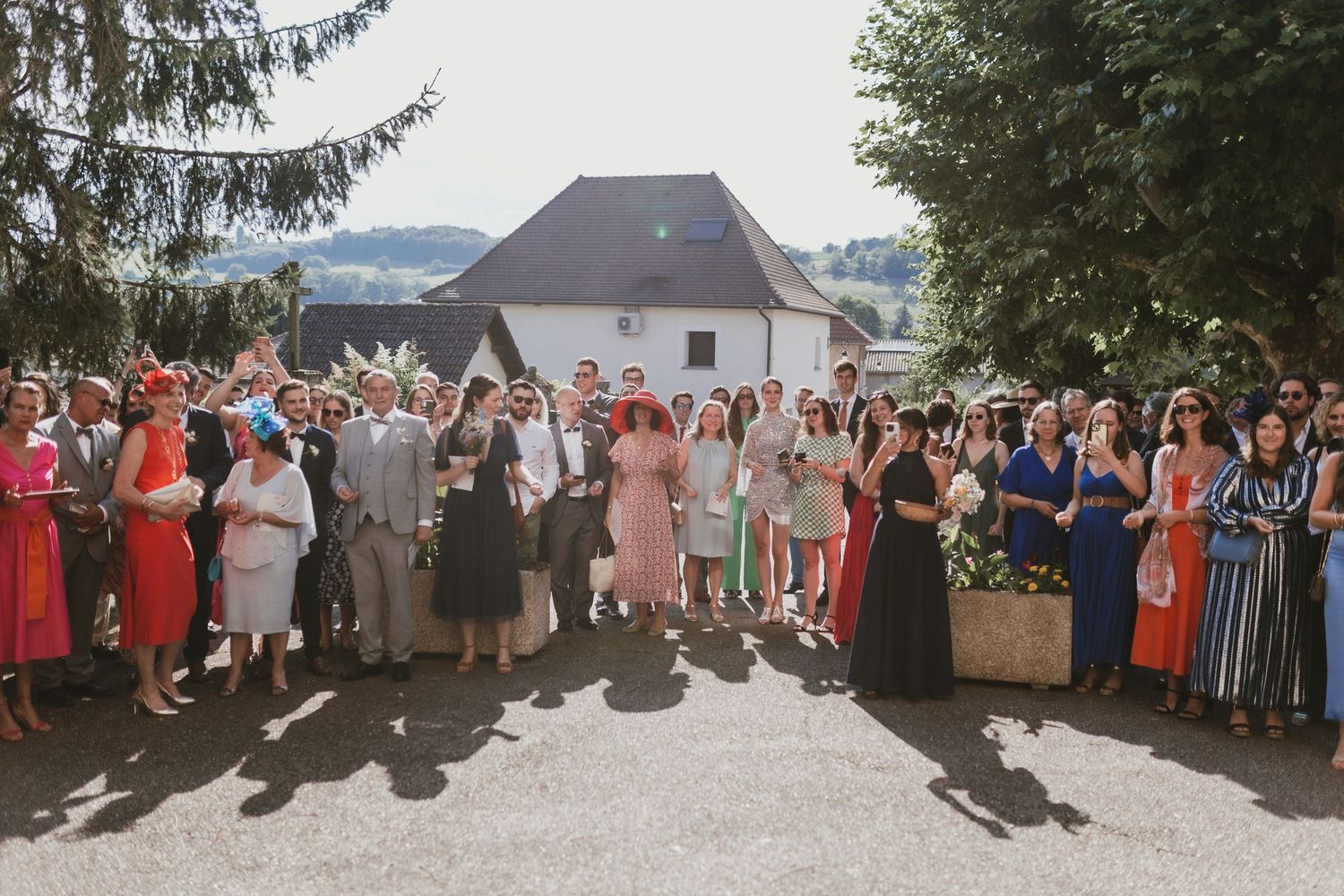 Large wedding group photo with guests in colorful attire gathered outside.