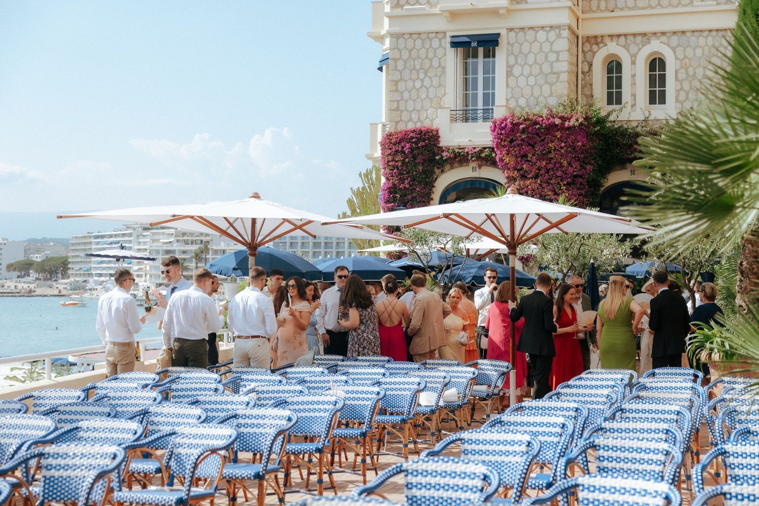 Blue and white striped lounge chairs line up beneath umbrellas at an oceanfront Mediterranean restaurant terrace.